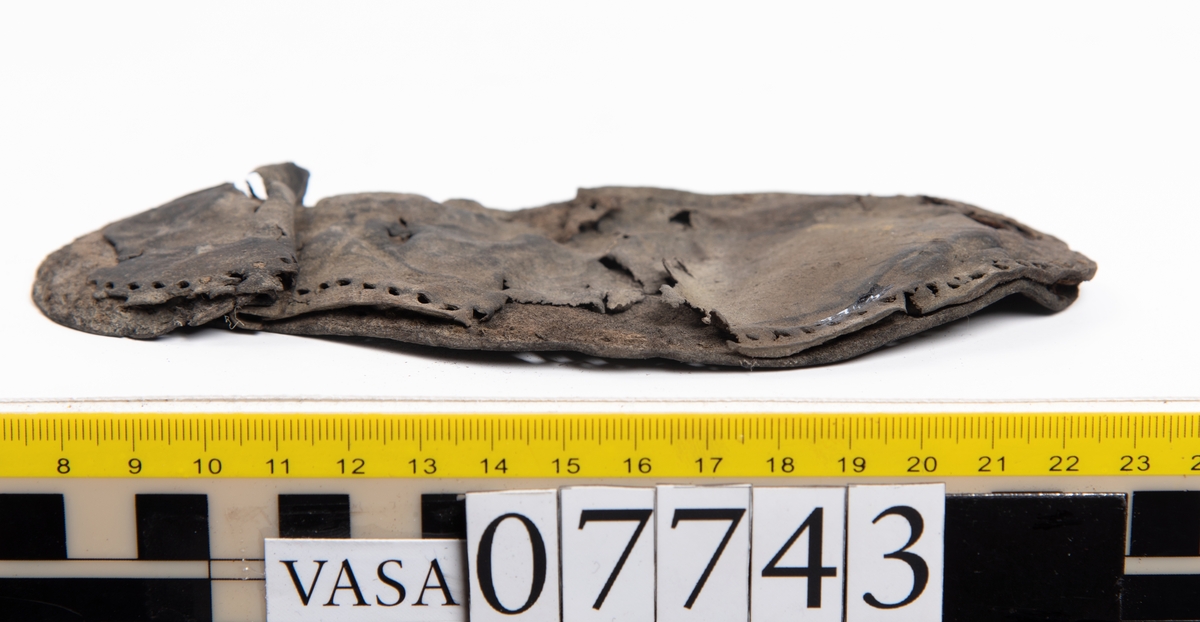 En sula. Sulan ligger vikt. Kvarsittande tråd samt hål efter skopligg. Lädret är spaltat. Två lösa mindre fragment.