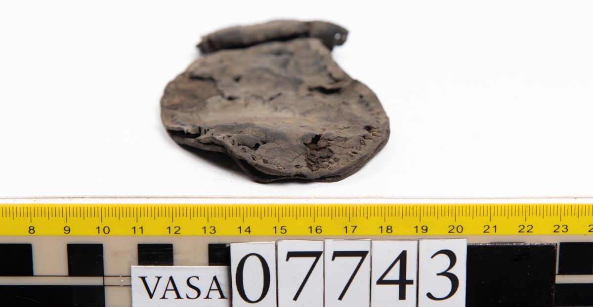 En sula. Sulan ligger vikt. Kvarsittande tråd samt hål efter skopligg. Lädret är spaltat. Två lösa mindre fragment.