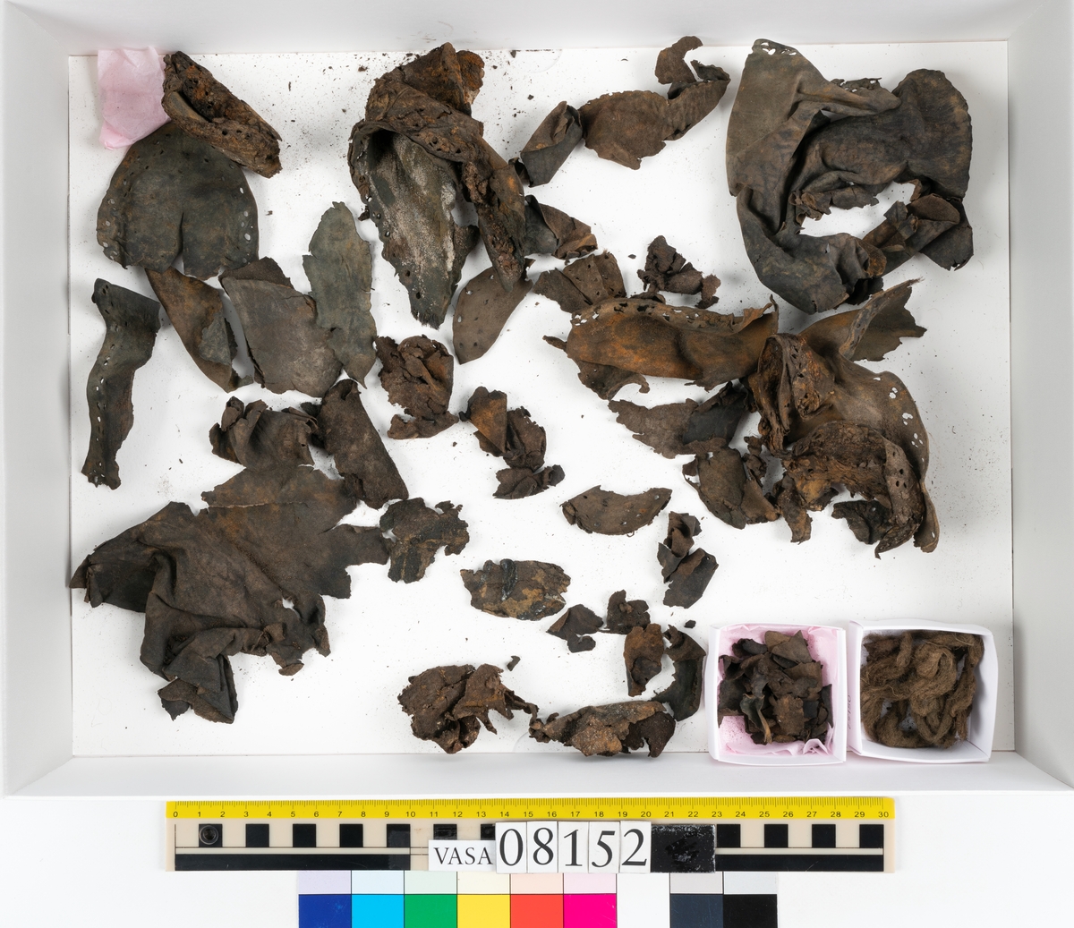 Ett femtiotal större och mindre delar och fragment från två stövlar: sulor, inlägg, ovanläder mm. Lädret ligger vikt. Bland delarna finns också en större klump av tråd eller snöre. Även ulltrådar.

Lädret är hårt och sprött samt har gul-vita utfällningar.