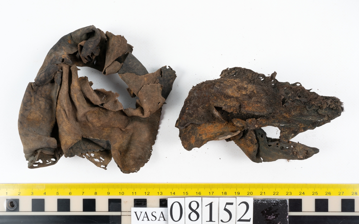 Ett femtiotal större och mindre delar och fragment från två stövlar: sulor, inlägg, ovanläder mm. Lädret ligger vikt. Bland delarna finns också en större klump av tråd eller snöre. Även ulltrådar.

Lädret är hårt och sprött samt har gul-vita utfällningar.