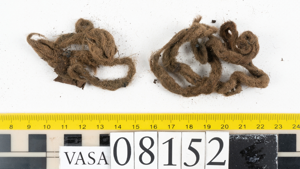 Ett femtiotal större och mindre delar och fragment från två stövlar: sulor, inlägg, ovanläder mm. Lädret ligger vikt. Bland delarna finns också en större klump av tråd eller snöre. Även ulltrådar.

Lädret är hårt och sprött samt har gul-vita utfällningar.