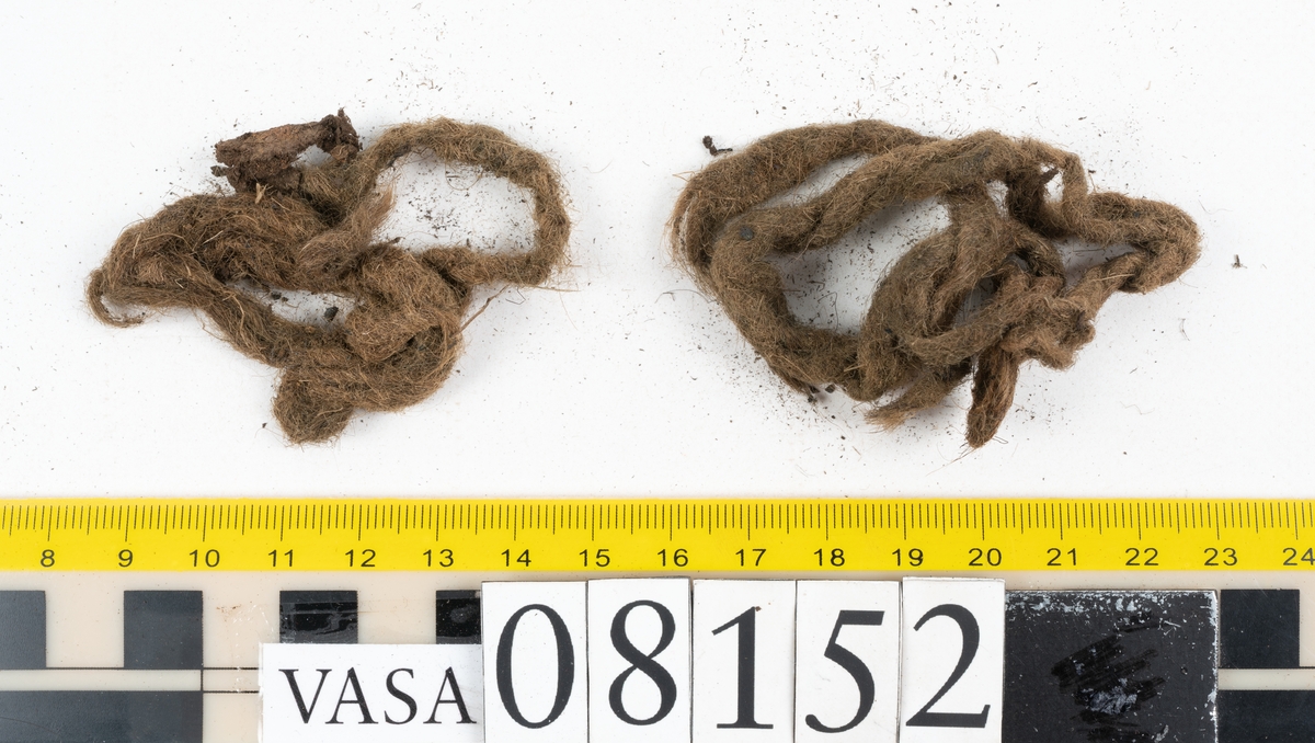 Ett femtiotal större och mindre delar och fragment från två stövlar: sulor, inlägg, ovanläder mm. Lädret ligger vikt. Bland delarna finns också en större klump av tråd eller snöre. Även ulltrådar.

Lädret är hårt och sprött samt har gul-vita utfällningar.
