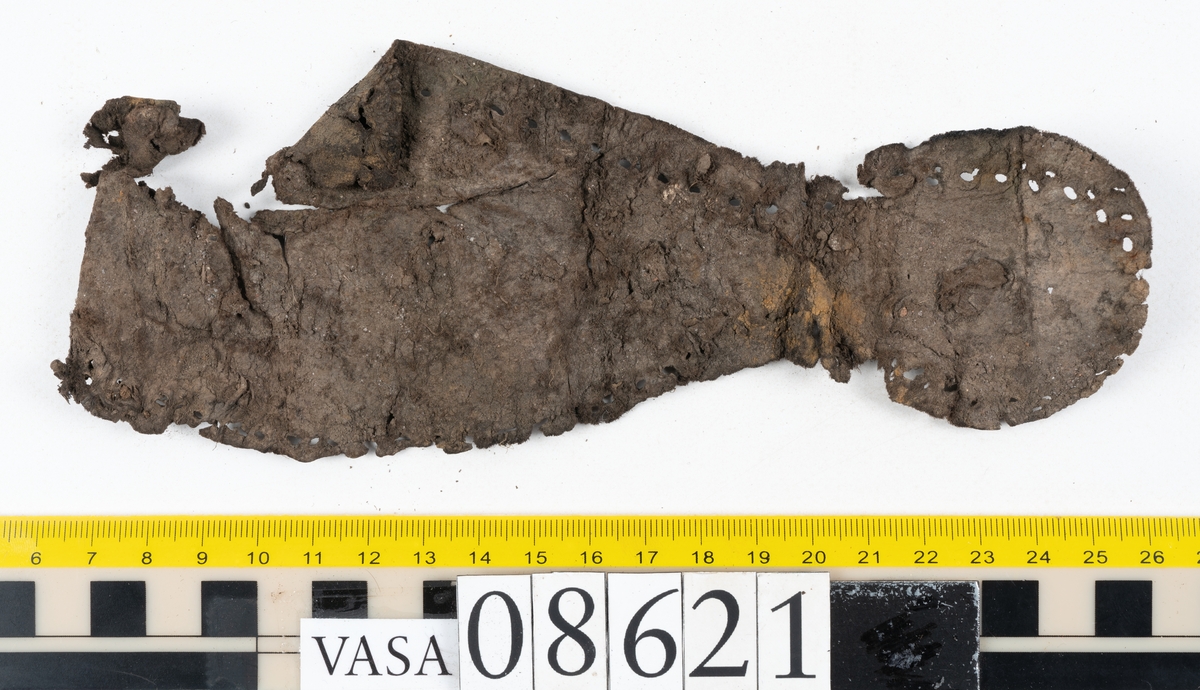 Delar och fragment från sko.
En fragmentarisk sula, fyndnummer 08621. Längs med ytterkanterna löper hål efter stygn. Lädret är spaltat och sprött.
En sula, fyndnummer 08621:1. Sulan är avskuren vid partiet för hålfoten. Sulan har hål efter stygn samt kvarsittande träpligg. Lädret är kraftigt.
En bakkappa, fyndnummer 08621:2. Bakkappan har suttit fästad på skons insida. Längs med ytterkanterna löper stygnshål med kvarsittande tråd.
Två klacklappar, fyndnummer 08621:3 och 08621:4. Klacklapparna har hål efter stygn och/eller träpligg.
Ett inlägg, fyndnummer 08621:5. Lädret är kraftigt.
Ett 100-tal fragment samt ytterligare två klacklappar och två inlägg.
En fragmentarisk bit tråd.
Tidigare även: Ett 15-tal fragment av textil. (Textilen fick ett eget fnr 27904 vid textildokumentationen 2015)