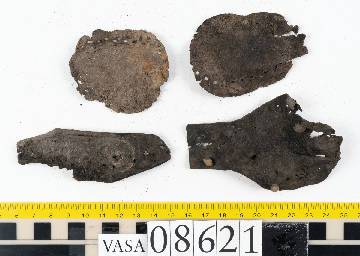 Delar och fragment från sko.
En fragmentarisk sula, fyndnummer 08621. Längs med ytterkanterna löper hål efter stygn. Lädret är spaltat och sprött.
En sula, fyndnummer 08621:1. Sulan är avskuren vid partiet för hålfoten. Sulan har hål efter stygn samt kvarsittande träpligg. Lädret är kraftigt.
En bakkappa, fyndnummer 08621:2. Bakkappan har suttit fästad på skons insida. Längs med ytterkanterna löper stygnshål med kvarsittande tråd.
Två klacklappar, fyndnummer 08621:3 och 08621:4. Klacklapparna har hål efter stygn och/eller träpligg.
Ett inlägg, fyndnummer 08621:5. Lädret är kraftigt.
Ett 100-tal fragment samt ytterligare två klacklappar och två inlägg.
En fragmentarisk bit tråd.
Tidigare även: Ett 15-tal fragment av textil. (Textilen fick ett eget fnr 27904 vid textildokumentationen 2015)