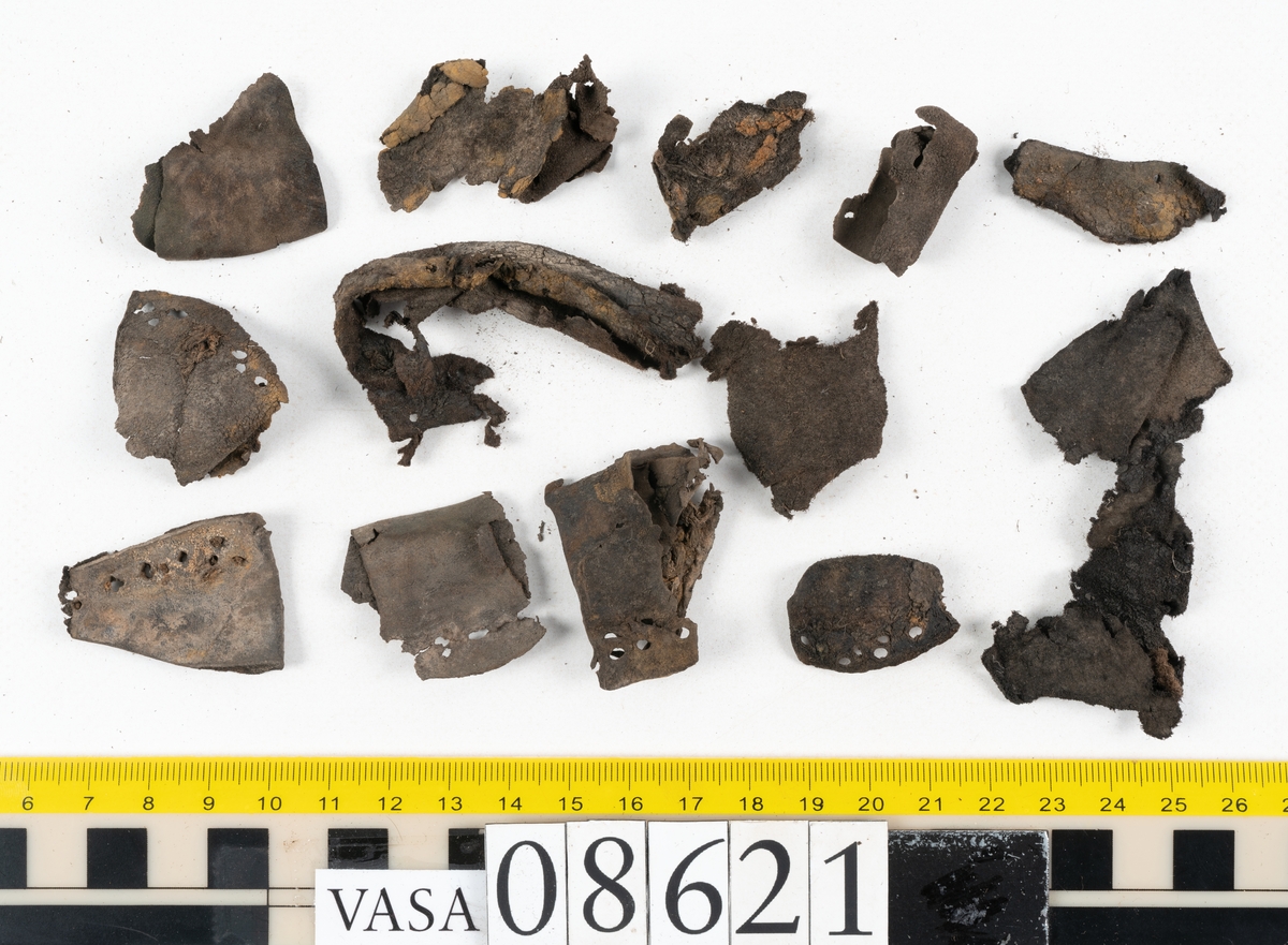 Delar och fragment från sko.
En fragmentarisk sula, fyndnummer 08621. Längs med ytterkanterna löper hål efter stygn. Lädret är spaltat och sprött.
En sula, fyndnummer 08621:1. Sulan är avskuren vid partiet för hålfoten. Sulan har hål efter stygn samt kvarsittande träpligg. Lädret är kraftigt.
En bakkappa, fyndnummer 08621:2. Bakkappan har suttit fästad på skons insida. Längs med ytterkanterna löper stygnshål med kvarsittande tråd.
Två klacklappar, fyndnummer 08621:3 och 08621:4. Klacklapparna har hål efter stygn och/eller träpligg.
Ett inlägg, fyndnummer 08621:5. Lädret är kraftigt.
Ett 100-tal fragment samt ytterligare två klacklappar och två inlägg.
En fragmentarisk bit tråd.
Tidigare även: Ett 15-tal fragment av textil. (Textilen fick ett eget fnr 27904 vid textildokumentationen 2015)