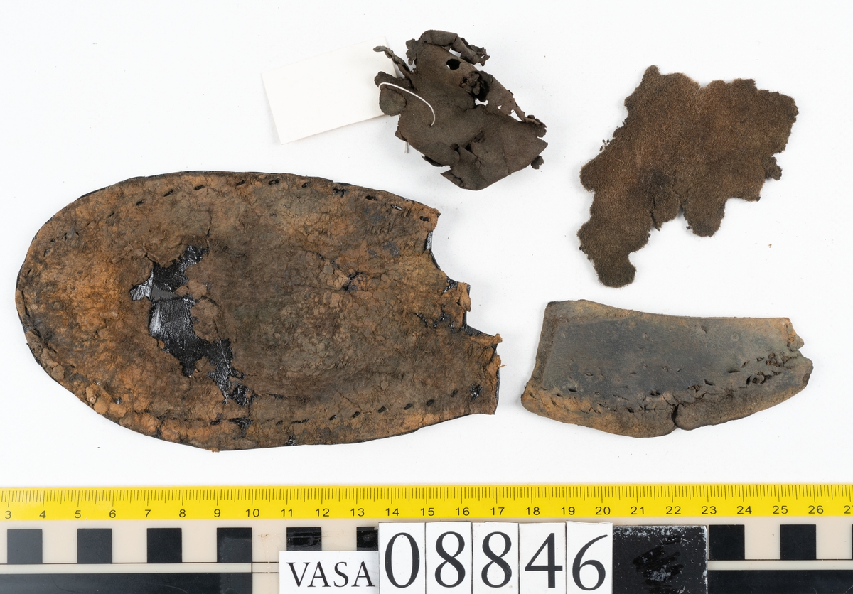 Läder samt en bit filtad textil.

Dokumentation 1996:
Delar av botten till holtrandsydd sko: del av botten, främre partiet av en löst liggande sula, två fragment, en laglapp samt skopligg.
Skobottnen består av en hel yttersula på vilken fyra klacklappar sitterfästade. Yttersulan har en ritsad linje som löper ca 5-15 mm in från sulkanten. På yttersulan sitter delar av sulor, troligtvis laglappar eller någon form av sulförstärkning, fästade med träpligg. Klacken består av fyra klacklappar. Mellan två av klacklapparna har en mindre kilformad lapp infogats. På klackbottnen sitter ett flertal större laglappar fästade med träpligg.
Den löst liggande delen av sulan är monterat på svart kartong.

Dokumentation 2022:
Skobotten. Tillverkad i läder. Skapades på en rak läst och bars på höger fot. Inga dekorationer. Den är sliten och har hål i yttersulan. Det finns tecken på att bäraren supinerade. Det finns spår av ett flertal lagningar med träpligg och en höjning av klacken. 
För mer information, se Uppritning under Länkade filer.

Text in english:
This is the bottom unit of shoe, made of leather, made on a straight last and worn on the right foot, with no decorative features. The bottom unit is worn, has small holes in the outer sole, and shows signs of supination. There have been extensive repairs including pegged repairs and a heel lift.
For more information, go to Länkade filer: Uppritning
