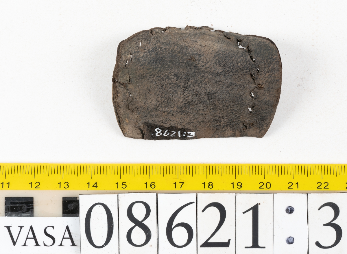 Delar och fragment från sko.
En fragmentarisk sula, fyndnummer 08621. Längs med ytterkanterna löper hål efter stygn. Lädret är spaltat och sprött.
En sula, fyndnummer 08621:1. Sulan är avskuren vid partiet för hålfoten. Sulan har hål efter stygn samt kvarsittande träpligg. Lädret är kraftigt.
En bakkappa, fyndnummer 08621:2. Bakkappan har suttit fästad på skons insida. Längs med ytterkanterna löper stygnshål med kvarsittande tråd.
Två klacklappar, fyndnummer 08621:3 och 08621:4. Klacklapparna har hål efter stygn och/eller träpligg.
Ett inlägg, fyndnummer 08621:5. Lädret är kraftigt.
Ett 100-tal fragment samt ytterligare två klacklappar och två inlägg.
En fragmentarisk bit tråd.
Tidigare även: Ett 15-tal fragment av textil. (Textilen fick ett eget fnr 27904 vid textildokumentationen 2015)