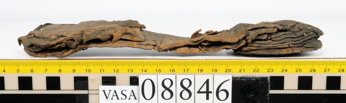Läder samt en bit filtad textil.

Dokumentation 1996:
Delar av botten till holtrandsydd sko: del av botten, främre partiet av en löst liggande sula, två fragment, en laglapp samt skopligg.
Skobottnen består av en hel yttersula på vilken fyra klacklappar sitterfästade. Yttersulan har en ritsad linje som löper ca 5-15 mm in från sulkanten. På yttersulan sitter delar av sulor, troligtvis laglappar eller någon form av sulförstärkning, fästade med träpligg. Klacken består av fyra klacklappar. Mellan två av klacklapparna har en mindre kilformad lapp infogats. På klackbottnen sitter ett flertal större laglappar fästade med träpligg.
Den löst liggande delen av sulan är monterat på svart kartong.

Dokumentation 2022:
Skobotten. Tillverkad i läder. Skapades på en rak läst och bars på höger fot. Inga dekorationer. Den är sliten och har hål i yttersulan. Det finns tecken på att bäraren supinerade. Det finns spår av ett flertal lagningar med träpligg och en höjning av klacken. 
För mer information, se Uppritning under Länkade filer.

Text in english:
This is the bottom unit of shoe, made of leather, made on a straight last and worn on the right foot, with no decorative features. The bottom unit is worn, has small holes in the outer sole, and shows signs of supination. There have been extensive repairs including pegged repairs and a heel lift.
For more information, go to Länkade filer: Uppritning