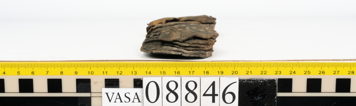 Läder samt en bit filtad textil.

Dokumentation 1996:
Delar av botten till holtrandsydd sko: del av botten, främre partiet av en löst liggande sula, två fragment, en laglapp samt skopligg.
Skobottnen består av en hel yttersula på vilken fyra klacklappar sitterfästade. Yttersulan har en ritsad linje som löper ca 5-15 mm in från sulkanten. På yttersulan sitter delar av sulor, troligtvis laglappar eller någon form av sulförstärkning, fästade med träpligg. Klacken består av fyra klacklappar. Mellan två av klacklapparna har en mindre kilformad lapp infogats. På klackbottnen sitter ett flertal större laglappar fästade med träpligg.
Den löst liggande delen av sulan är monterat på svart kartong.

Dokumentation 2022:
Skobotten. Tillverkad i läder. Skapades på en rak läst och bars på höger fot. Inga dekorationer. Den är sliten och har hål i yttersulan. Det finns tecken på att bäraren supinerade. Det finns spår av ett flertal lagningar med träpligg och en höjning av klacken. 
För mer information, se Uppritning under Länkade filer.

Text in english:
This is the bottom unit of shoe, made of leather, made on a straight last and worn on the right foot, with no decorative features. The bottom unit is worn, has small holes in the outer sole, and shows signs of supination. There have been extensive repairs including pegged repairs and a heel lift.
For more information, go to Länkade filer: Uppritning