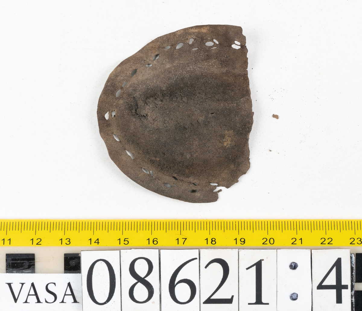 Delar och fragment från sko.
En fragmentarisk sula, fyndnummer 08621. Längs med ytterkanterna löper hål efter stygn. Lädret är spaltat och sprött.
En sula, fyndnummer 08621:1. Sulan är avskuren vid partiet för hålfoten. Sulan har hål efter stygn samt kvarsittande träpligg. Lädret är kraftigt.
En bakkappa, fyndnummer 08621:2. Bakkappan har suttit fästad på skons insida. Längs med ytterkanterna löper stygnshål med kvarsittande tråd.
Två klacklappar, fyndnummer 08621:3 och 08621:4. Klacklapparna har hål efter stygn och/eller träpligg.
Ett inlägg, fyndnummer 08621:5. Lädret är kraftigt.
Ett 100-tal fragment samt ytterligare två klacklappar och två inlägg.
En fragmentarisk bit tråd.
Tidigare även: Ett 15-tal fragment av textil. (Textilen fick ett eget fnr 27904 vid textildokumentationen 2015)