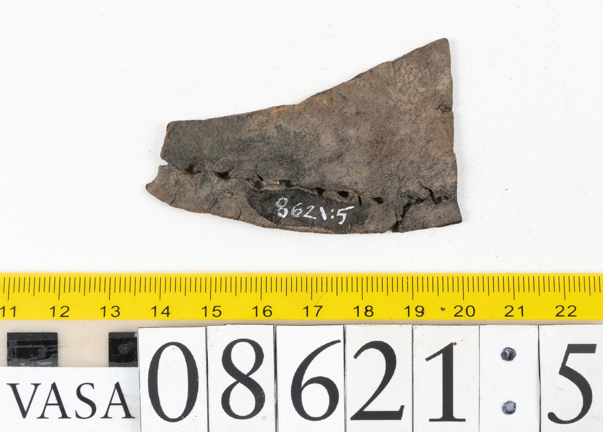 Delar och fragment från sko.
En fragmentarisk sula, fyndnummer 08621. Längs med ytterkanterna löper hål efter stygn. Lädret är spaltat och sprött.
En sula, fyndnummer 08621:1. Sulan är avskuren vid partiet för hålfoten. Sulan har hål efter stygn samt kvarsittande träpligg. Lädret är kraftigt.
En bakkappa, fyndnummer 08621:2. Bakkappan har suttit fästad på skons insida. Längs med ytterkanterna löper stygnshål med kvarsittande tråd.
Två klacklappar, fyndnummer 08621:3 och 08621:4. Klacklapparna har hål efter stygn och/eller träpligg.
Ett inlägg, fyndnummer 08621:5. Lädret är kraftigt.
Ett 100-tal fragment samt ytterligare två klacklappar och två inlägg.
En fragmentarisk bit tråd.
Tidigare även: Ett 15-tal fragment av textil. (Textilen fick ett eget fnr 27904 vid textildokumentationen 2015)