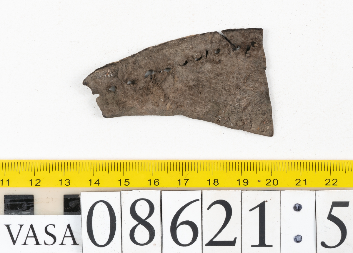Delar och fragment från sko.
En fragmentarisk sula, fyndnummer 08621. Längs med ytterkanterna löper hål efter stygn. Lädret är spaltat och sprött.
En sula, fyndnummer 08621:1. Sulan är avskuren vid partiet för hålfoten. Sulan har hål efter stygn samt kvarsittande träpligg. Lädret är kraftigt.
En bakkappa, fyndnummer 08621:2. Bakkappan har suttit fästad på skons insida. Längs med ytterkanterna löper stygnshål med kvarsittande tråd.
Två klacklappar, fyndnummer 08621:3 och 08621:4. Klacklapparna har hål efter stygn och/eller träpligg.
Ett inlägg, fyndnummer 08621:5. Lädret är kraftigt.
Ett 100-tal fragment samt ytterligare två klacklappar och två inlägg.
En fragmentarisk bit tråd.
Tidigare även: Ett 15-tal fragment av textil. (Textilen fick ett eget fnr 27904 vid textildokumentationen 2015)