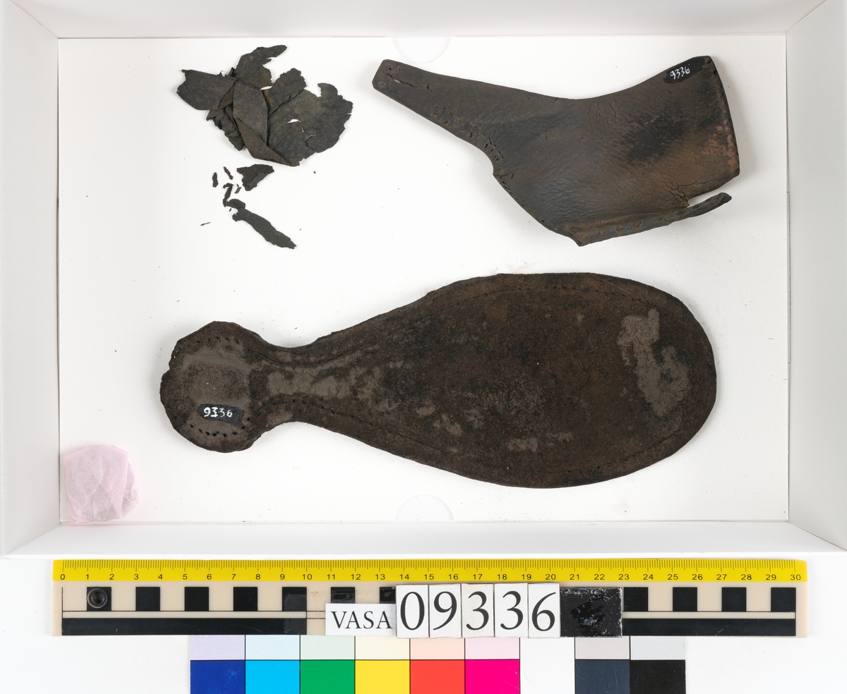 Fyra delar från sko: en sula, ett sidostycke med slejf samt två ospecificerade fragment.

En ritsad linje löper strax innanför sulans ytterkant. På sulans köttsida finns kvarsittande tråd. I änden på sidostyckets slejf syns ett runt hål med en nedskärning. På sidostycket syns kvarsittande tråd. Lädret är kraftigt.