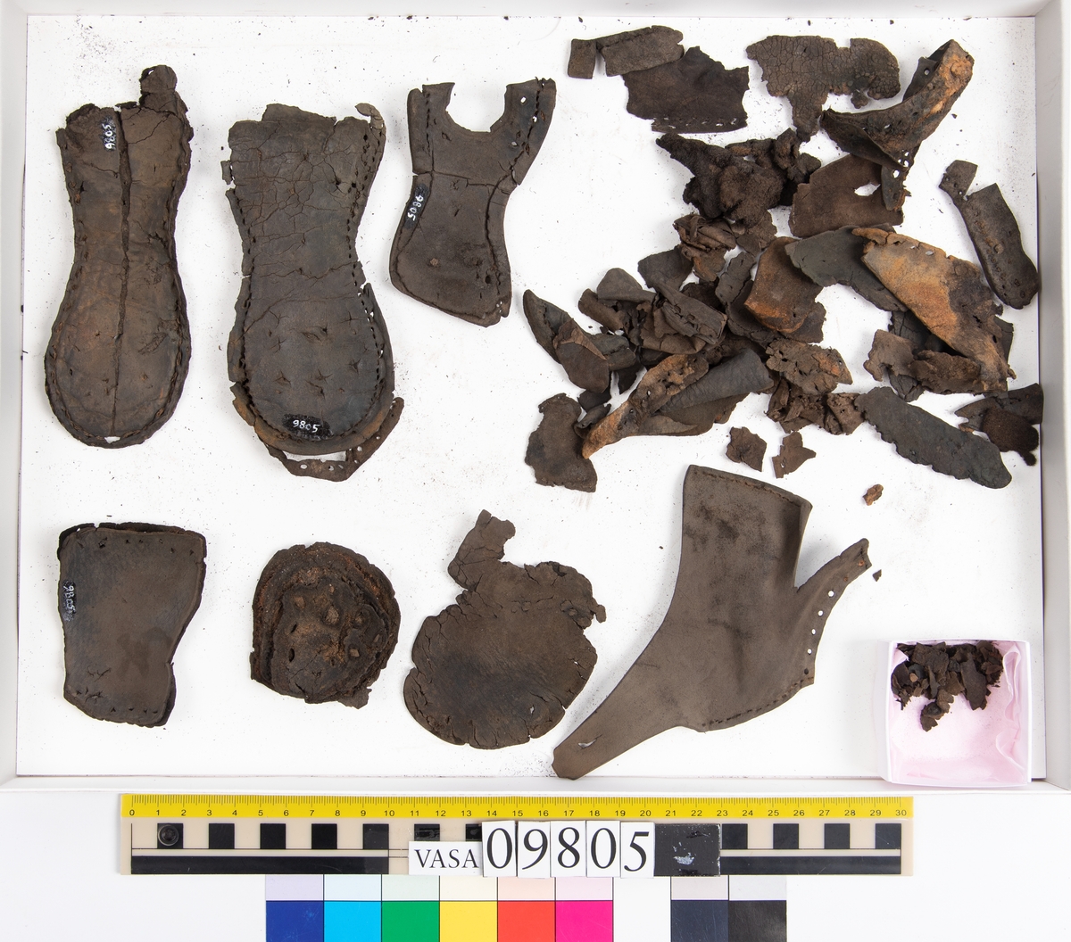 Ett 60-tal delar och fragment från sko: sulor, sidostycke, delar från klack m.m. samt ett filtfragment. Bland delarna kan urskiljas en klacklapp med kvarsittande skopligg samt ett sidostycke med slejf. I slejfänden finns ett hål - troligtvis knapphål.

Delar av lädret är kraftigt och välbevarat medan andra delar är spaltade samt har rostliknande utfällningar.
