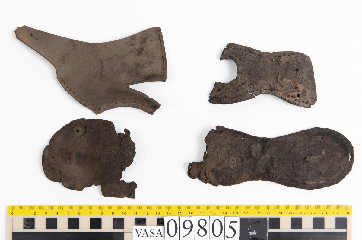 Ett 60-tal delar och fragment från sko: sulor, sidostycke, delar från klack m.m. samt ett filtfragment. Bland delarna kan urskiljas en klacklapp med kvarsittande skopligg samt ett sidostycke med slejf. I slejfänden finns ett hål - troligtvis knapphål.

Delar av lädret är kraftigt och välbevarat medan andra delar är spaltade samt har rostliknande utfällningar.