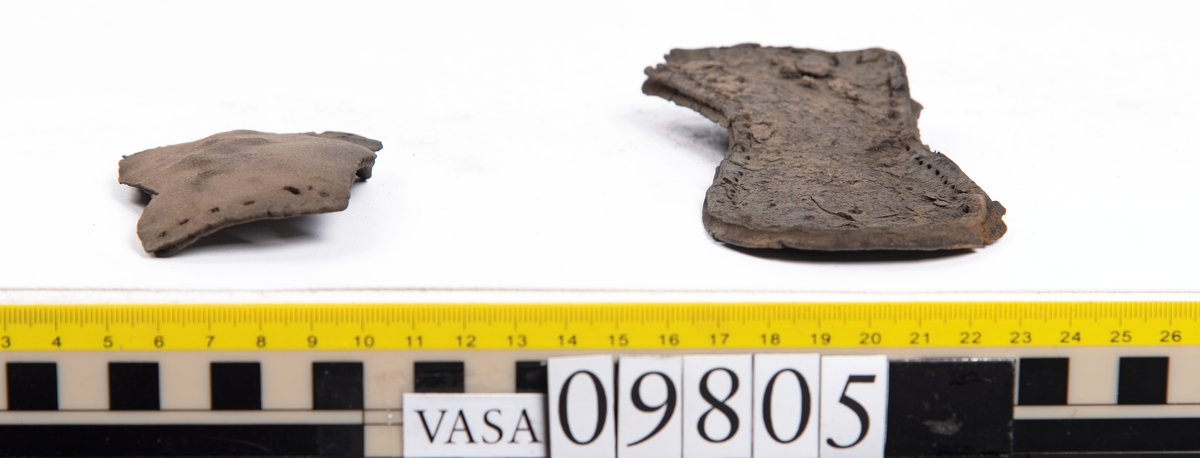 Ett 60-tal delar och fragment från sko: sulor, sidostycke, delar från klack m.m. samt ett filtfragment. Bland delarna kan urskiljas en klacklapp med kvarsittande skopligg samt ett sidostycke med slejf. I slejfänden finns ett hål - troligtvis knapphål.

Delar av lädret är kraftigt och välbevarat medan andra delar är spaltade samt har rostliknande utfällningar.
