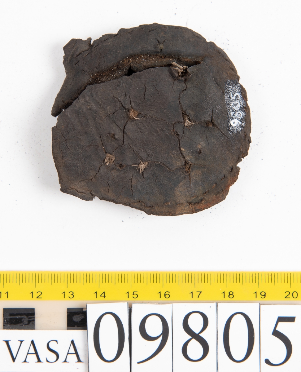 Ett 60-tal delar och fragment från sko: sulor, sidostycke, delar från klack m.m. samt ett filtfragment. Bland delarna kan urskiljas en klacklapp med kvarsittande skopligg samt ett sidostycke med slejf. I slejfänden finns ett hål - troligtvis knapphål.

Delar av lädret är kraftigt och välbevarat medan andra delar är spaltade samt har rostliknande utfällningar.