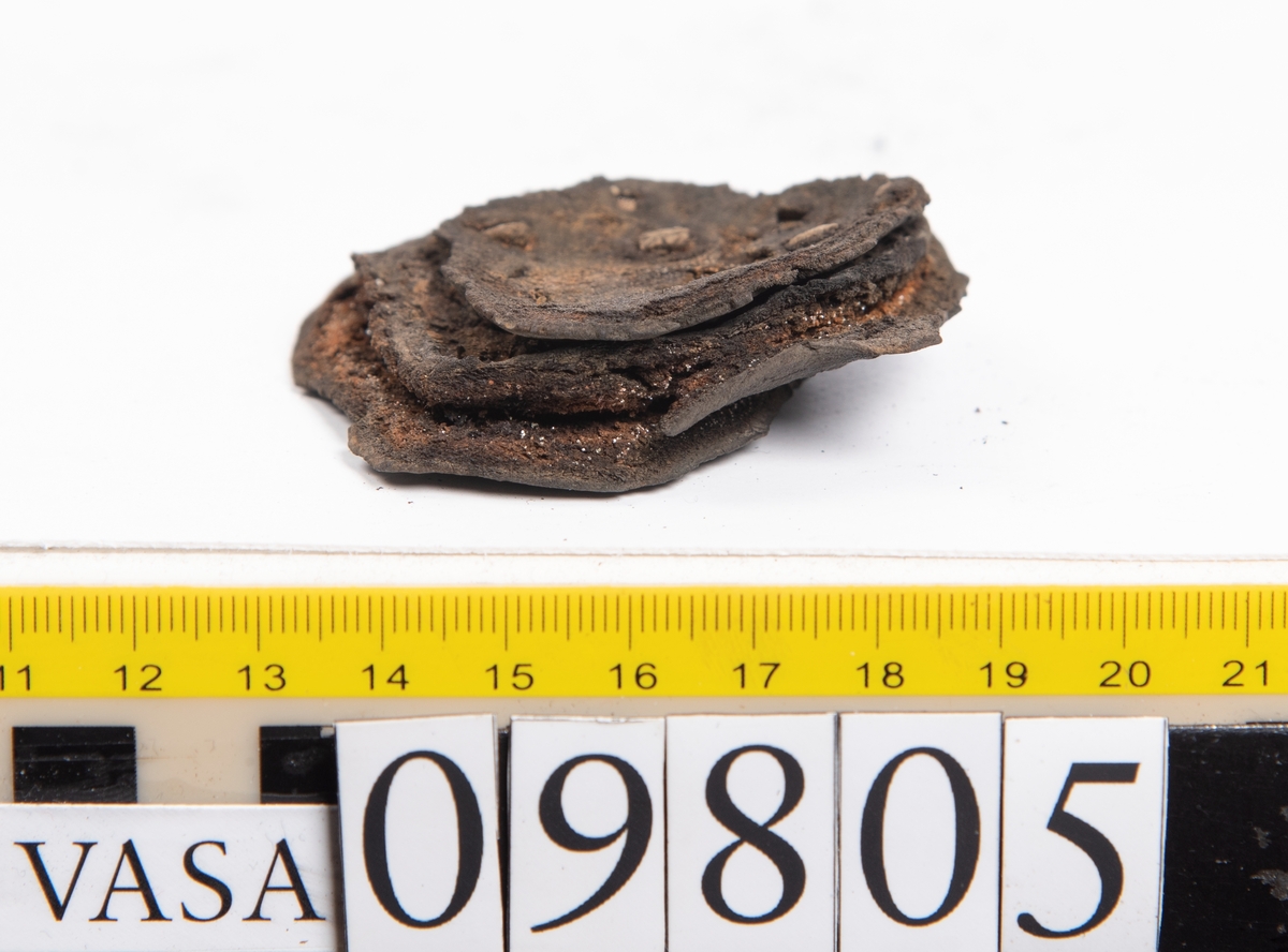 Ett 60-tal delar och fragment från sko: sulor, sidostycke, delar från klack m.m. samt ett filtfragment. Bland delarna kan urskiljas en klacklapp med kvarsittande skopligg samt ett sidostycke med slejf. I slejfänden finns ett hål - troligtvis knapphål.

Delar av lädret är kraftigt och välbevarat medan andra delar är spaltade samt har rostliknande utfällningar.