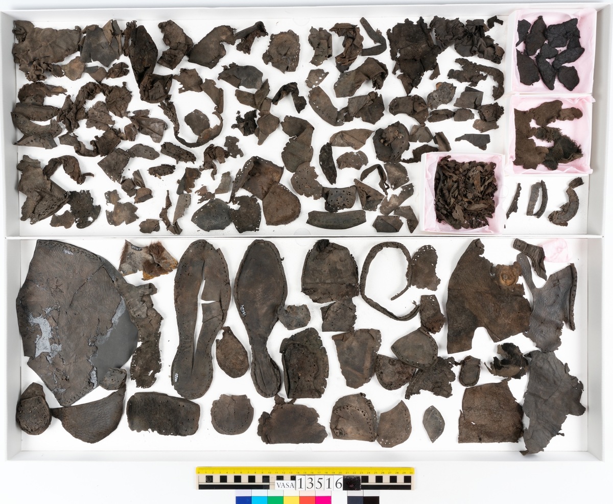 Dokumentation 1997:
Ett tvåhundrafemtiotal delar och fragment från skor: sulor, klacklappar, inlägg, ovanläder mm.
Sula fyndnummer 13516. Längs med sulans ytterkant finns hål efter träpligg och tråd. På sulans mitt finns en ritsad skåra i sulans längdriktning. Lädret är kraftigt.
Sula fyndnummer 13516:1. Sulan härrör troligtvis från en annan sko än sula 13516, bl a då man ser till mått samt hur den har varit fästad till botten. Längs med ytterkanterna syns kvarsittande tråd. Lädret är kraftigt.
Ovanläder fyndnummer 13516:2. Ovanlädret är monterat på svart kartong.
Sidostycke med slejf, fyndnummer 13516:3. I slejfänden finns ett runt snörhål.
Del av klack, fyndnummer 13516:4. Klacken består av fyra klacklappar och har kvarsittande träpligg.
Skuren läderbit med kvarsittande hår, fyndnummer 13516:5. Läderbiten är troligtvis ett inlägg. Lädret har rostfärgade utfällningar.
På några av delarna syns kvarsittande tråd och träpligg. Även träflisor samt 12 filtbitar och en bit tuskaftsväv.
Lädret varierar vad gäller kvalitet och kondition. Flertalet delar är spaltade och mycket spröda.

Dokumentation 2022:
Del av ovanläder. Bakkappa till en öppen svensksko. Tillverkad i läder. Inga dekorationer. Delaminerad.
13516:1 är en bindsula. Tillverkad i läder. Skapades på en rak läst och bars på höger fot. Inga dekorationer. Den har ett flertal hål. Det finns inga tecken på lagningar. 
För mer information, se Uppritning under Länkade filer.

Text in english:
This is a quarter of an open sided shoe, made of leather of stitch-down construction, with no decorative features but delaminated.
13516:1 is the insole of a shoe, made of leather, made on a right last and worn on the right foot, with no decorative features. There are holes in the insole but no signs of repairs.
For more information, go to Länkade filer: Uppritning