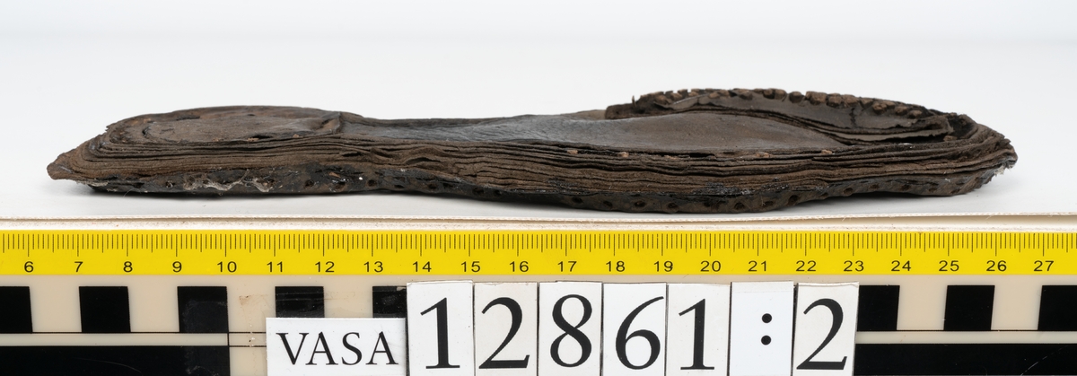 Två monterade stövlar samt delar och fragment från stövel. Eventuellt omfattar fyndnumret även delar och fragment från sko.
Stövel till höger fot, fyndnummer 12861.
Skaftet är skuret i ett stycke som har fästs samman med en söm på baksidan av stöveln. Skaftets övre del är något solfjädersformad, troligtvis för att det skall kunna vikas ned. Stövelskaftets övre del är något fragmentariskt. Ovanlädret är skuret i ett stycke. Skaftets insida har förstärkts med svart kartong av konserveringsenheten. Ovanlädret är monterat på svart kartong.
Stövelbottnen består av spaltade sulor. På bottnens högra sida finns en laglapp med kvarsittande träpligg. På insidan av stöveln är hälen förstärkt med en bakkappa. Bottnen tycks inte vara komplett.
Sulorna har fästs samman med tråd och lim av konserveringsenheten.
Stövel till vänster fot, fyndnummer 12861:1.
Skaftet är skuret i ett stycke som har fästs samman med en söm på baksidan av stöveln av konserveringsenheten. Skaftets övre del är något solfjädersformad, troligtvis för att det skall kunna vikas ned. Ovanlädret är skuret i ett stycke. Stöveln är något bättre bevarad än fyndnummer 12861. Stövelbottnen, fyndnummer 12861:2 ligger löst.
Botten till vänster stövel, fyndnummer 12861:2.
Stövelbottnen består av spaltade sulor samt en spaltad klacklapp. Sulorna är ritsade. Längs med ytterkanterna löper hål efter stygn och kvarsittande träpligg. På bottnens vänstra sida finns en laglapp med kvarsittande träpligg. Bottnen tycks inte vara komplett. Sulorna har fästs samman med tråd och lim av konserverinsenheten.
Ett 130-tal delar och fragment från stövel, varav vissa delar möjligen härrör från skor.
Bland delarna och fragmenten går bl a att urskilja sex stycken sulor, en del av en klack med kvarsittande träpligg, femton klacklappar, sju delar av inlägg, elva skurna läderremsor, nio träpligg samt en tråd eller ett snöre i form av tvinnad ull. Minst tre av sulorna härrör från höger stövelbotten. Troligtvis härrör de andra tre sulorna från vänster stövelbotten. Längs med de skurna läderremsornas ytterkanter löper hål efter stygn.
Delar av lädret är spaltat och mycket sprött.
Innehåller även textilfragment.