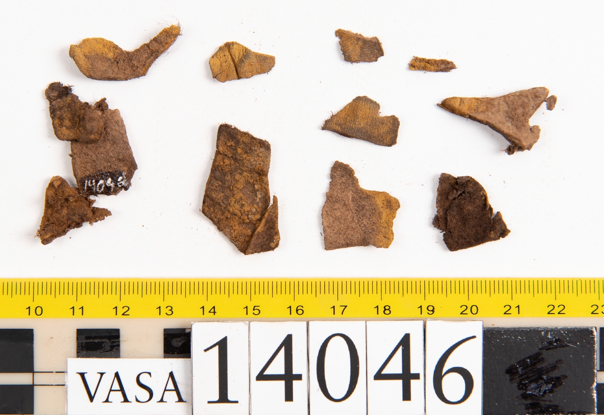 Tjugo ospecificerade läderbitar samt ett flertal mycket små fragment. På två av fragmenten, fyndnummer 14046:1 samt 14046:7, finns svarta hårstrån, ca 5-20 mm långa. Lädret saknar hål efter stygn eller träpligg.
