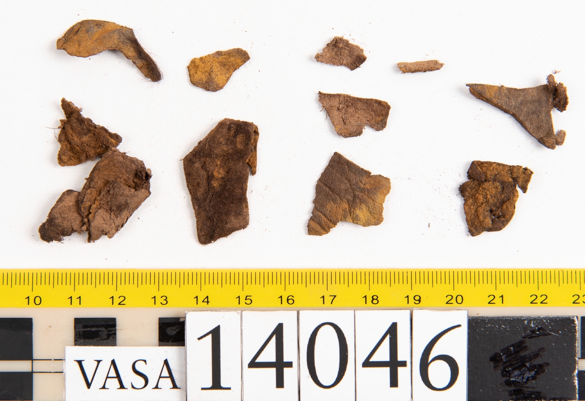 Tjugo ospecificerade läderbitar samt ett flertal mycket små fragment. På två av fragmenten, fyndnummer 14046:1 samt 14046:7, finns svarta hårstrån, ca 5-20 mm långa. Lädret saknar hål efter stygn eller träpligg.