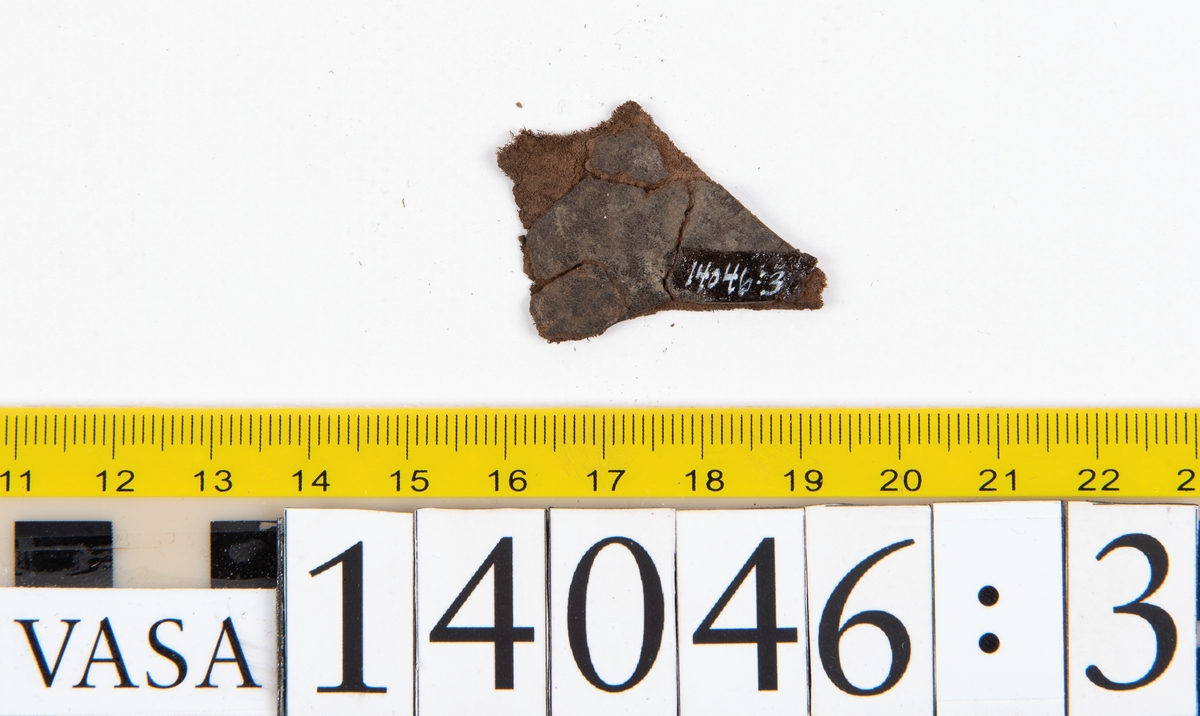 Tjugo ospecificerade läderbitar samt ett flertal mycket små fragment. På två av fragmenten, fyndnummer 14046:1 samt 14046:7, finns svarta hårstrån, ca 5-20 mm långa. Lädret saknar hål efter stygn eller träpligg.