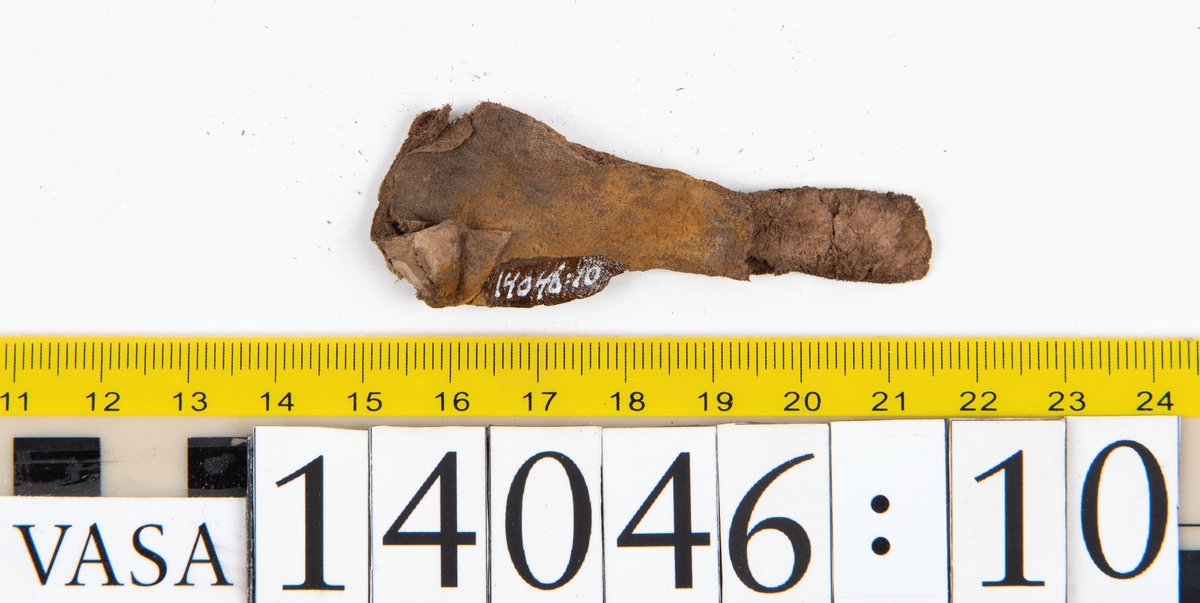 Tjugo ospecificerade läderbitar samt ett flertal mycket små fragment. På två av fragmenten, fyndnummer 14046:1 samt 14046:7, finns svarta hårstrån, ca 5-20 mm långa. Lädret saknar hål efter stygn eller träpligg.