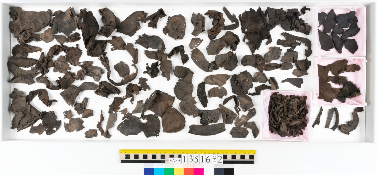 Dokumentation 1997:
Ett tvåhundrafemtiotal delar och fragment från skor: sulor, klacklappar, inlägg, ovanläder mm.
Sula fyndnummer 13516. Längs med sulans ytterkant finns hål efter träpligg och tråd. På sulans mitt finns en ritsad skåra i sulans längdriktning. Lädret är kraftigt.
Sula fyndnummer 13516:1. Sulan härrör troligtvis från en annan sko än sula 13516, bl a då man ser till mått samt hur den har varit fästad till botten. Längs med ytterkanterna syns kvarsittande tråd. Lädret är kraftigt.
Ovanläder fyndnummer 13516:2. Ovanlädret är monterat på svart kartong.
Sidostycke med slejf, fyndnummer 13516:3. I slejfänden finns ett runt snörhål.
Del av klack, fyndnummer 13516:4. Klacken består av fyra klacklappar och har kvarsittande träpligg.
Skuren läderbit med kvarsittande hår, fyndnummer 13516:5. Läderbiten är troligtvis ett inlägg. Lädret har rostfärgade utfällningar.
På några av delarna syns kvarsittande tråd och träpligg. Även träflisor samt 12 filtbitar och en bit tuskaftsväv.
Lädret varierar vad gäller kvalitet och kondition. Flertalet delar är spaltade och mycket spröda.

Dokumentation 2022:
Del av ovanläder. Bakkappa till en öppen svensksko. Tillverkad i läder. Inga dekorationer. Delaminerad.
13516:1 är en bindsula. Tillverkad i läder. Skapades på en rak läst och bars på höger fot. Inga dekorationer. Den har ett flertal hål. Det finns inga tecken på lagningar. 
För mer information, se Uppritning under Länkade filer.

Text in english:
This is a quarter of an open sided shoe, made of leather of stitch-down construction, with no decorative features but delaminated.
13516:1 is the insole of a shoe, made of leather, made on a right last and worn on the right foot, with no decorative features. There are holes in the insole but no signs of repairs.
For more information, go to Länkade filer: Uppritning