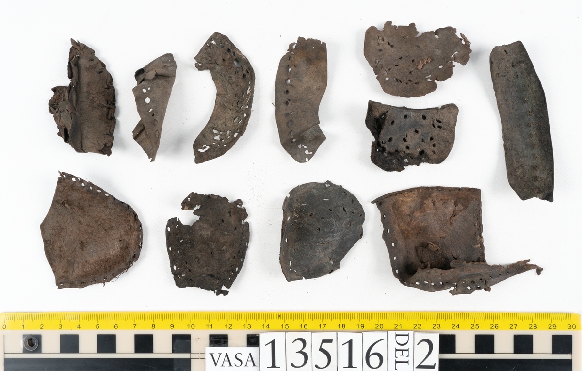 Dokumentation 1997:
Ett tvåhundrafemtiotal delar och fragment från skor: sulor, klacklappar, inlägg, ovanläder mm.
Sula fyndnummer 13516. Längs med sulans ytterkant finns hål efter träpligg och tråd. På sulans mitt finns en ritsad skåra i sulans längdriktning. Lädret är kraftigt.
Sula fyndnummer 13516:1. Sulan härrör troligtvis från en annan sko än sula 13516, bl a då man ser till mått samt hur den har varit fästad till botten. Längs med ytterkanterna syns kvarsittande tråd. Lädret är kraftigt.
Ovanläder fyndnummer 13516:2. Ovanlädret är monterat på svart kartong.
Sidostycke med slejf, fyndnummer 13516:3. I slejfänden finns ett runt snörhål.
Del av klack, fyndnummer 13516:4. Klacken består av fyra klacklappar och har kvarsittande träpligg.
Skuren läderbit med kvarsittande hår, fyndnummer 13516:5. Läderbiten är troligtvis ett inlägg. Lädret har rostfärgade utfällningar.
På några av delarna syns kvarsittande tråd och träpligg. Även träflisor samt 12 filtbitar och en bit tuskaftsväv.
Lädret varierar vad gäller kvalitet och kondition. Flertalet delar är spaltade och mycket spröda.

Dokumentation 2022:
Del av ovanläder. Bakkappa till en öppen svensksko. Tillverkad i läder. Inga dekorationer. Delaminerad.
13516:1 är en bindsula. Tillverkad i läder. Skapades på en rak läst och bars på höger fot. Inga dekorationer. Den har ett flertal hål. Det finns inga tecken på lagningar. 
För mer information, se Uppritning under Länkade filer.

Text in english:
This is a quarter of an open sided shoe, made of leather of stitch-down construction, with no decorative features but delaminated.
13516:1 is the insole of a shoe, made of leather, made on a right last and worn on the right foot, with no decorative features. There are holes in the insole but no signs of repairs.
For more information, go to Länkade filer: Uppritning