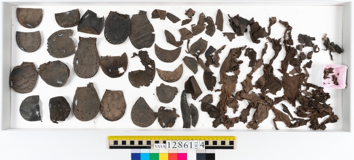 Två monterade stövlar samt delar och fragment från stövel. Eventuellt omfattar fyndnumret även delar och fragment från sko.
Stövel till höger fot, fyndnummer 12861.
Skaftet är skuret i ett stycke som har fästs samman med en söm på baksidan av stöveln. Skaftets övre del är något solfjädersformad, troligtvis för att det skall kunna vikas ned. Stövelskaftets övre del är något fragmentariskt. Ovanlädret är skuret i ett stycke. Skaftets insida har förstärkts med svart kartong av konserveringsenheten. Ovanlädret är monterat på svart kartong.
Stövelbottnen består av spaltade sulor. På bottnens högra sida finns en laglapp med kvarsittande träpligg. På insidan av stöveln är hälen förstärkt med en bakkappa. Bottnen tycks inte vara komplett.
Sulorna har fästs samman med tråd och lim av konserveringsenheten.
Stövel till vänster fot, fyndnummer 12861:1.
Skaftet är skuret i ett stycke som har fästs samman med en söm på baksidan av stöveln av konserveringsenheten. Skaftets övre del är något solfjädersformad, troligtvis för att det skall kunna vikas ned. Ovanlädret är skuret i ett stycke. Stöveln är något bättre bevarad än fyndnummer 12861. Stövelbottnen, fyndnummer 12861:2 ligger löst.
Botten till vänster stövel, fyndnummer 12861:2.
Stövelbottnen består av spaltade sulor samt en spaltad klacklapp. Sulorna är ritsade. Längs med ytterkanterna löper hål efter stygn och kvarsittande träpligg. På bottnens vänstra sida finns en laglapp med kvarsittande träpligg. Bottnen tycks inte vara komplett. Sulorna har fästs samman med tråd och lim av konserverinsenheten.
Ett 130-tal delar och fragment från stövel, varav vissa delar möjligen härrör från skor.
Bland delarna och fragmenten går bl a att urskilja sex stycken sulor, en del av en klack med kvarsittande träpligg, femton klacklappar, sju delar av inlägg, elva skurna läderremsor, nio träpligg samt en tråd eller ett snöre i form av tvinnad ull. Minst tre av sulorna härrör från höger stövelbotten. Troligtvis härrör de andra tre sulorna från vänster stövelbotten. Längs med de skurna läderremsornas ytterkanter löper hål efter stygn.
Delar av lädret är spaltat och mycket sprött.
Innehåller även textilfragment.