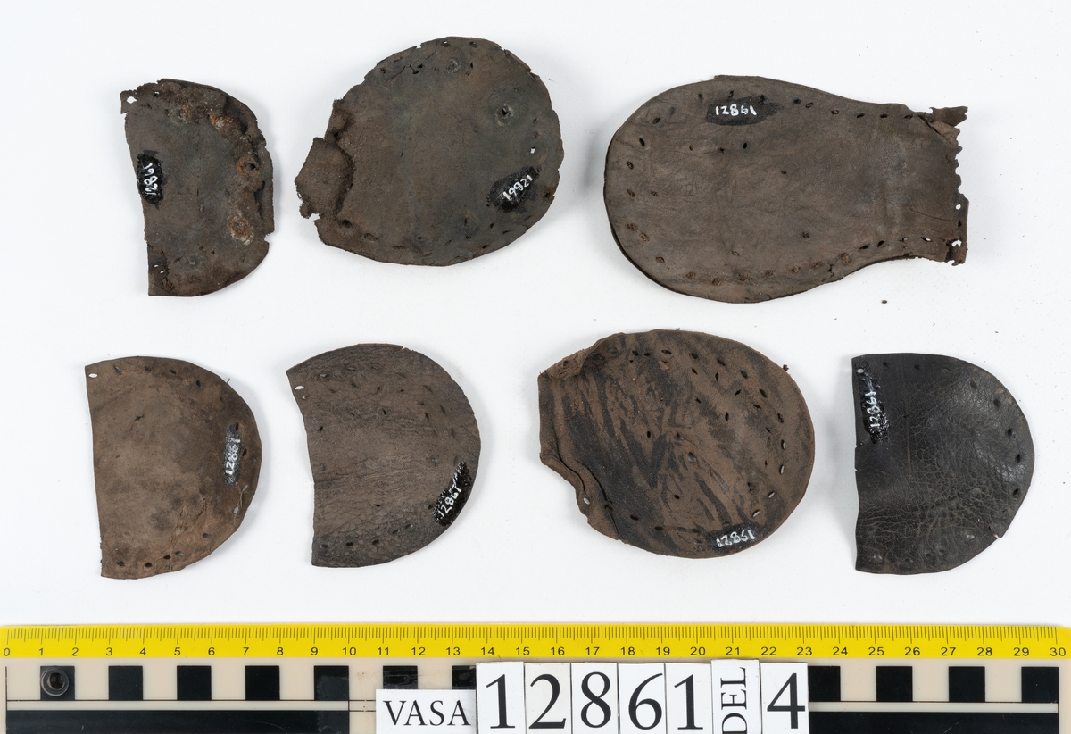 Två monterade stövlar samt delar och fragment från stövel. Eventuellt omfattar fyndnumret även delar och fragment från sko.
Stövel till höger fot, fyndnummer 12861.
Skaftet är skuret i ett stycke som har fästs samman med en söm på baksidan av stöveln. Skaftets övre del är något solfjädersformad, troligtvis för att det skall kunna vikas ned. Stövelskaftets övre del är något fragmentariskt. Ovanlädret är skuret i ett stycke. Skaftets insida har förstärkts med svart kartong av konserveringsenheten. Ovanlädret är monterat på svart kartong.
Stövelbottnen består av spaltade sulor. På bottnens högra sida finns en laglapp med kvarsittande träpligg. På insidan av stöveln är hälen förstärkt med en bakkappa. Bottnen tycks inte vara komplett.
Sulorna har fästs samman med tråd och lim av konserveringsenheten.
Stövel till vänster fot, fyndnummer 12861:1.
Skaftet är skuret i ett stycke som har fästs samman med en söm på baksidan av stöveln av konserveringsenheten. Skaftets övre del är något solfjädersformad, troligtvis för att det skall kunna vikas ned. Ovanlädret är skuret i ett stycke. Stöveln är något bättre bevarad än fyndnummer 12861. Stövelbottnen, fyndnummer 12861:2 ligger löst.
Botten till vänster stövel, fyndnummer 12861:2.
Stövelbottnen består av spaltade sulor samt en spaltad klacklapp. Sulorna är ritsade. Längs med ytterkanterna löper hål efter stygn och kvarsittande träpligg. På bottnens vänstra sida finns en laglapp med kvarsittande träpligg. Bottnen tycks inte vara komplett. Sulorna har fästs samman med tråd och lim av konserverinsenheten.
Ett 130-tal delar och fragment från stövel, varav vissa delar möjligen härrör från skor.
Bland delarna och fragmenten går bl a att urskilja sex stycken sulor, en del av en klack med kvarsittande träpligg, femton klacklappar, sju delar av inlägg, elva skurna läderremsor, nio träpligg samt en tråd eller ett snöre i form av tvinnad ull. Minst tre av sulorna härrör från höger stövelbotten. Troligtvis härrör de andra tre sulorna från vänster stövelbotten. Längs med de skurna läderremsornas ytterkanter löper hål efter stygn.
Delar av lädret är spaltat och mycket sprött.
Innehåller även textilfragment.
