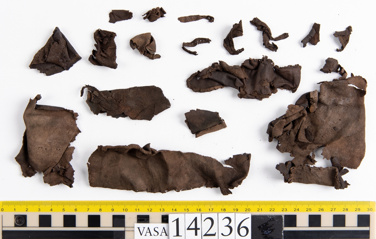 Ett 50-tal läderfragment av kraghandske eller kragvante. På lädret syns hål efter stygn.