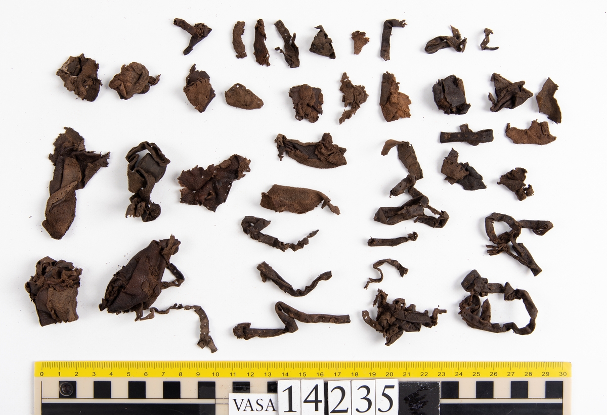 Ett 60-tal fragment från handske. På flera av fragmenten finns hål efter stygn. Lädret är mycket mjukt, tunt och sprött.