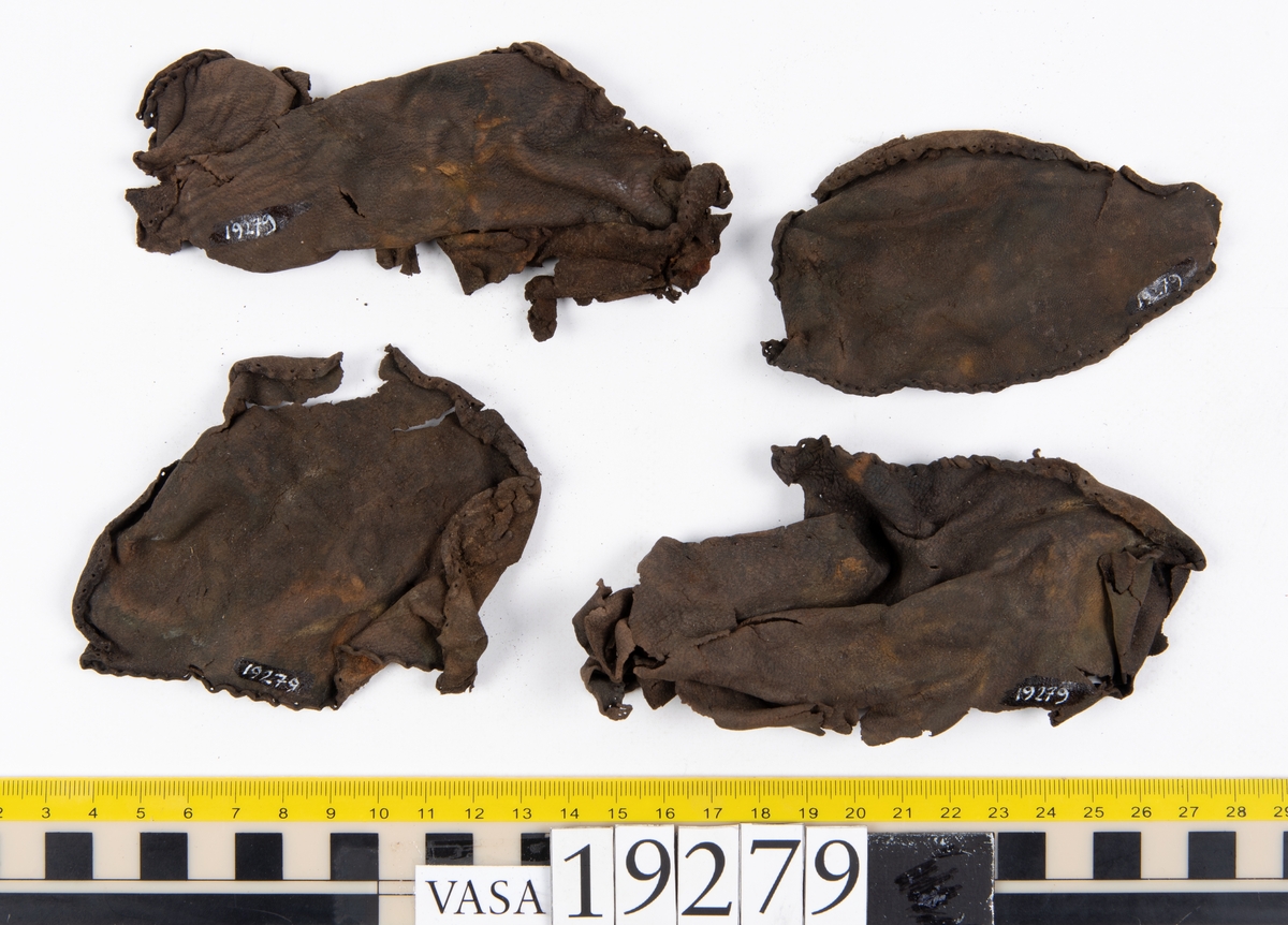 Tjugosex, ospecificerade läderfragment. Längs med ytterkanterna på fyra av de större fragmenten syns hål efter stygn. Stygnen sitter med 3 mm mellanrum. Lädret är tunt och mycket sprött.