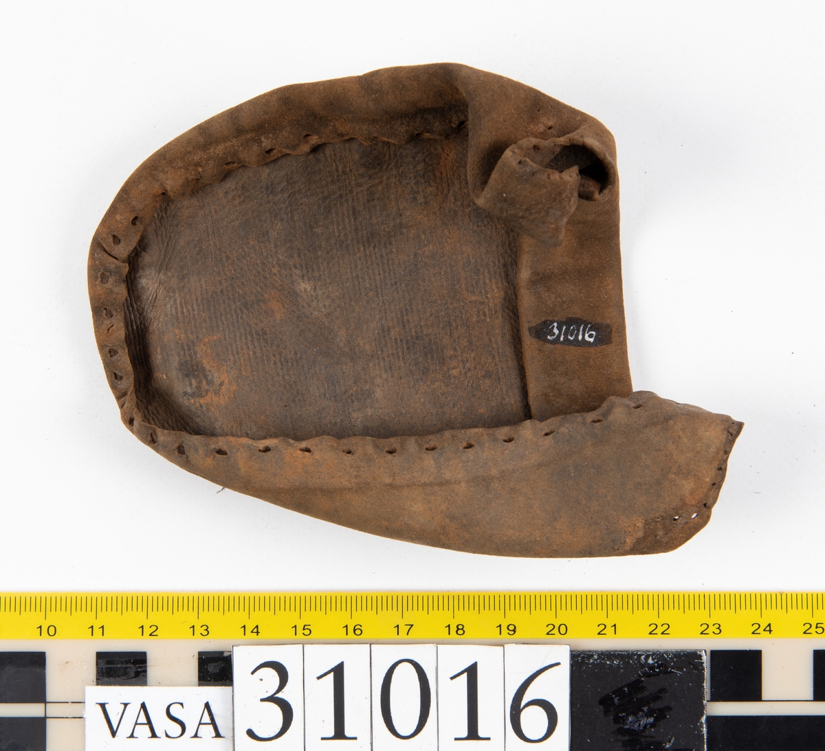 Ovanläder och bakkappa till sko. Längs med ovanlädrets ytterkant löper en enkel rad med stygnshål. Narvytan är välbevarad och har en rutmönstrad struktur. Bakkappans nedre kant är vikt. Kanten har legat invikt och suttit fästad i sulpaketet.