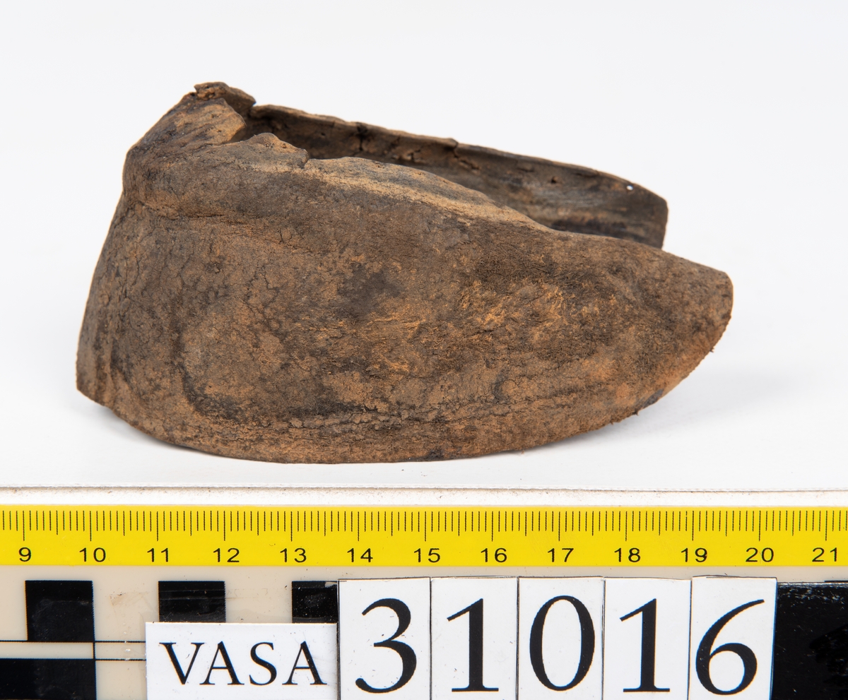 Ovanläder och bakkappa till sko. Längs med ovanlädrets ytterkant löper en enkel rad med stygnshål. Narvytan är välbevarad och har en rutmönstrad struktur. Bakkappans nedre kant är vikt. Kanten har legat invikt och suttit fästad i sulpaketet.