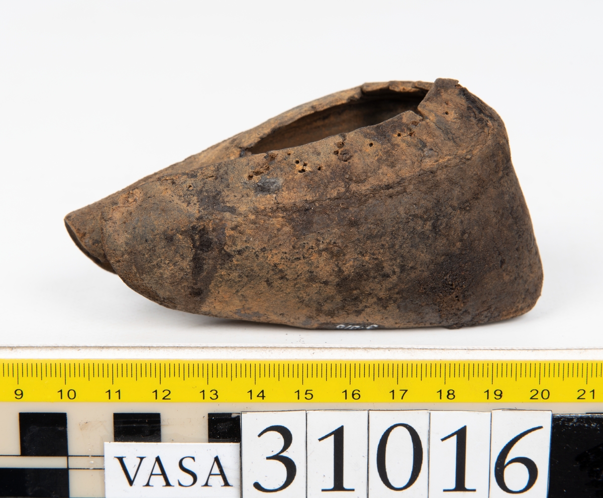 Ovanläder och bakkappa till sko. Längs med ovanlädrets ytterkant löper en enkel rad med stygnshål. Narvytan är välbevarad och har en rutmönstrad struktur. Bakkappans nedre kant är vikt. Kanten har legat invikt och suttit fästad i sulpaketet.