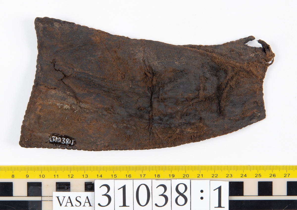 Delar av en väska. Totalt rör det sig om fyra delar, varav två lösa delar av en läderrem.
Halvcirkelformat skuret läderstycke, fyndnummer 31038. Troligtvis utgör läderstycket en del av bottnen och sidostycket till en väska.  Längs med ytterkanten syns ritsade skåror som är ritsade två och två. Genom skårorna löper en, ca 20 mm bred, läderrem. Remmen har troligtvis fungerat som axelrem, eventuellt livrem. Ena änden av remmen är dubbelvikt. Där remmen vikts finns ett runt hål. Kring hålet finns intryck och rostliknande utfällningar, troligtvis efter ett spänne. På motsatta sidan syns hål efter stygn som löper i formen av en rektangel. På läderstyckets nedre del finns runda, hårda, grönfärgade blåsor.
Delar av läderstycket är fragmentariskt eller saknas och lädret har rostfärgade utfällningar.
Sidostycke eller del av lock till en väska, fyndnummer 31038:1. Lädret är skuret i ett rektangulärt stycke. Runt ytterkanterna löper stygnshål. I ett av hörnen finns en rektangulär skåra. På läderstycket syns svaga intryck i form av cirklar.
Del av rem, fyndnummer 31038:2. I ena änden finns stygnshål som löper i formen av en rektangel.
Del av rem, fyndnummer 31038:3. Remmen dubbelvikt och tycks sakna stygnshål.
Lädret är på det hela taget kraftigt och välbevarat.