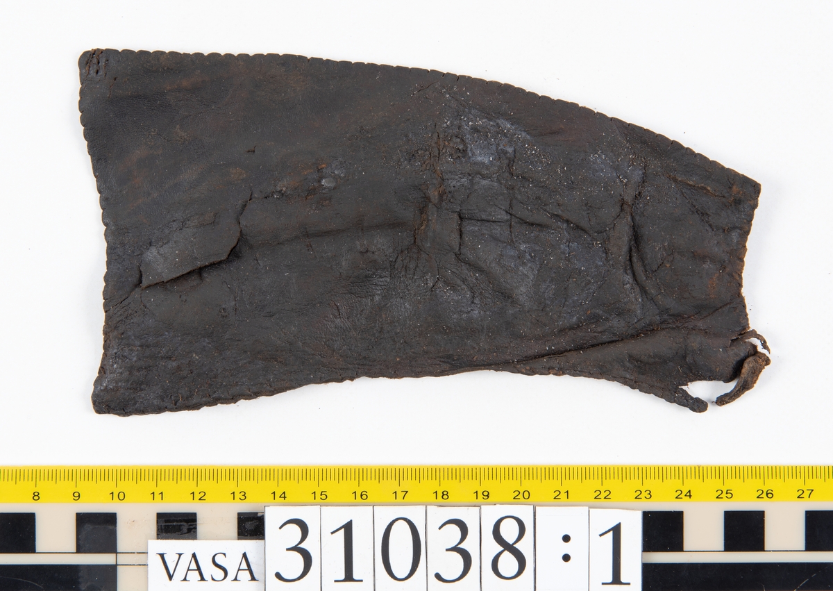 Delar av en väska. Totalt rör det sig om fyra delar, varav två lösa delar av en läderrem.
Halvcirkelformat skuret läderstycke, fyndnummer 31038. Troligtvis utgör läderstycket en del av bottnen och sidostycket till en väska.  Längs med ytterkanten syns ritsade skåror som är ritsade två och två. Genom skårorna löper en, ca 20 mm bred, läderrem. Remmen har troligtvis fungerat som axelrem, eventuellt livrem. Ena änden av remmen är dubbelvikt. Där remmen vikts finns ett runt hål. Kring hålet finns intryck och rostliknande utfällningar, troligtvis efter ett spänne. På motsatta sidan syns hål efter stygn som löper i formen av en rektangel. På läderstyckets nedre del finns runda, hårda, grönfärgade blåsor.
Delar av läderstycket är fragmentariskt eller saknas och lädret har rostfärgade utfällningar.
Sidostycke eller del av lock till en väska, fyndnummer 31038:1. Lädret är skuret i ett rektangulärt stycke. Runt ytterkanterna löper stygnshål. I ett av hörnen finns en rektangulär skåra. På läderstycket syns svaga intryck i form av cirklar.
Del av rem, fyndnummer 31038:2. I ena änden finns stygnshål som löper i formen av en rektangel.
Del av rem, fyndnummer 31038:3. Remmen dubbelvikt och tycks sakna stygnshål.
Lädret är på det hela taget kraftigt och välbevarat.