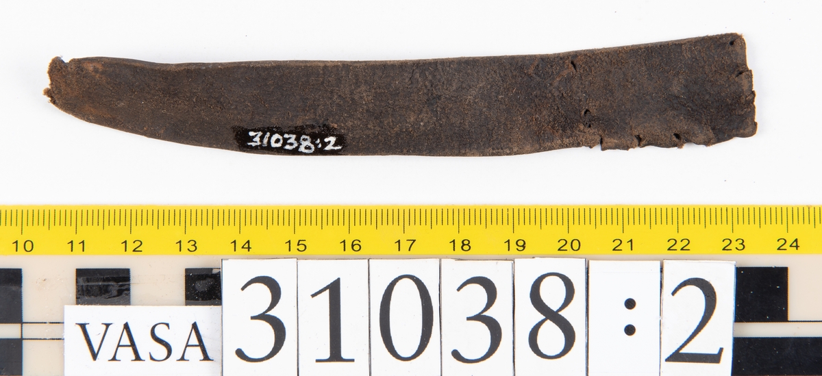 Delar av en väska. Totalt rör det sig om fyra delar, varav två lösa delar av en läderrem.
Halvcirkelformat skuret läderstycke, fyndnummer 31038. Troligtvis utgör läderstycket en del av bottnen och sidostycket till en väska.  Längs med ytterkanten syns ritsade skåror som är ritsade två och två. Genom skårorna löper en, ca 20 mm bred, läderrem. Remmen har troligtvis fungerat som axelrem, eventuellt livrem. Ena änden av remmen är dubbelvikt. Där remmen vikts finns ett runt hål. Kring hålet finns intryck och rostliknande utfällningar, troligtvis efter ett spänne. På motsatta sidan syns hål efter stygn som löper i formen av en rektangel. På läderstyckets nedre del finns runda, hårda, grönfärgade blåsor.
Delar av läderstycket är fragmentariskt eller saknas och lädret har rostfärgade utfällningar.
Sidostycke eller del av lock till en väska, fyndnummer 31038:1. Lädret är skuret i ett rektangulärt stycke. Runt ytterkanterna löper stygnshål. I ett av hörnen finns en rektangulär skåra. På läderstycket syns svaga intryck i form av cirklar.
Del av rem, fyndnummer 31038:2. I ena änden finns stygnshål som löper i formen av en rektangel.
Del av rem, fyndnummer 31038:3. Remmen dubbelvikt och tycks sakna stygnshål.
Lädret är på det hela taget kraftigt och välbevarat.