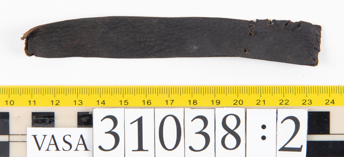 Delar av en väska. Totalt rör det sig om fyra delar, varav två lösa delar av en läderrem.
Halvcirkelformat skuret läderstycke, fyndnummer 31038. Troligtvis utgör läderstycket en del av bottnen och sidostycket till en väska.  Längs med ytterkanten syns ritsade skåror som är ritsade två och två. Genom skårorna löper en, ca 20 mm bred, läderrem. Remmen har troligtvis fungerat som axelrem, eventuellt livrem. Ena änden av remmen är dubbelvikt. Där remmen vikts finns ett runt hål. Kring hålet finns intryck och rostliknande utfällningar, troligtvis efter ett spänne. På motsatta sidan syns hål efter stygn som löper i formen av en rektangel. På läderstyckets nedre del finns runda, hårda, grönfärgade blåsor.
Delar av läderstycket är fragmentariskt eller saknas och lädret har rostfärgade utfällningar.
Sidostycke eller del av lock till en väska, fyndnummer 31038:1. Lädret är skuret i ett rektangulärt stycke. Runt ytterkanterna löper stygnshål. I ett av hörnen finns en rektangulär skåra. På läderstycket syns svaga intryck i form av cirklar.
Del av rem, fyndnummer 31038:2. I ena änden finns stygnshål som löper i formen av en rektangel.
Del av rem, fyndnummer 31038:3. Remmen dubbelvikt och tycks sakna stygnshål.
Lädret är på det hela taget kraftigt och välbevarat.