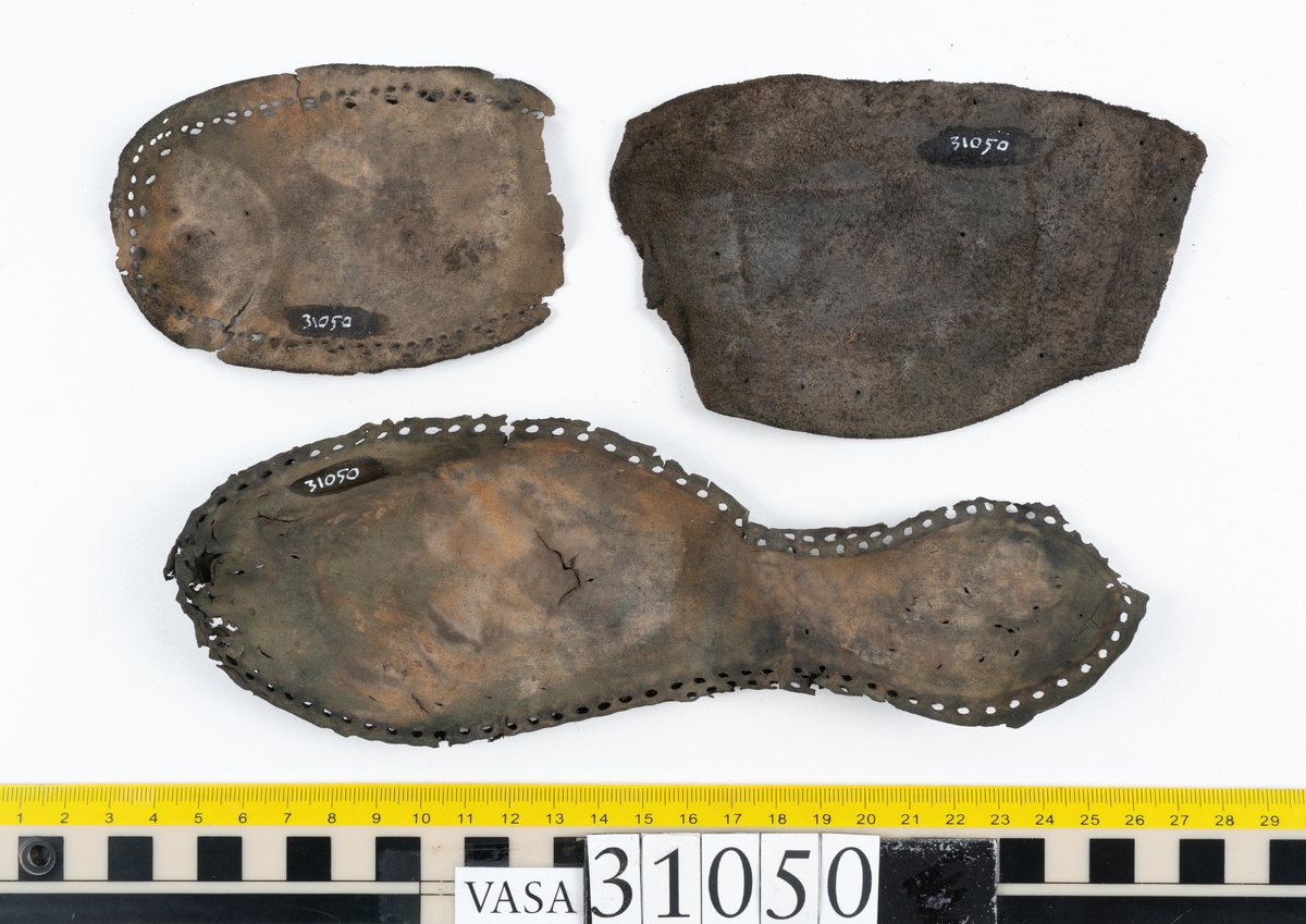 Dokumentation 1997:
Delar och fragment från sko.
Fyra sulor, fyndnummer 31050, 31050:1, 310502 samt 31050:4. Runt sulornas ytterkanter löper hål efter stygns och träpligg. Två av sulorna, fyndnummer 31050 och 31050:1, är spaltade. Lädret är mycket sprött. Sulor fyndnummer 31050:2 och 31050:3 består av ett relativt kraftigt läder. Sula fyndnummer 31050:3 är avskuren vid tåpartiet. Eventuellt kandenna sula härröra från en annan skobotten.
En bakkappa, fyndnummer 31050:4. Längs med ytterkanterna löper stygnshål. lädret är spaltat och sprött.
Ett 40-tal delar och fragment av sulor, inlägg, ovanläder mm.

Även växtfibrer.

Dokumentation 2022:
Bindsula till en svensksko. Tillverkad i läder. Inga dekorationer. Hör ihop med fyndnummer 11317. Framdelen saknas. Sättet bäraren använde skon tyder på att hen hade metatarsalgi. Det finns inga tecken på lagningar. 
För mer information, se Länkade filer: Uppritning

Text in english:
This is the insole of a shoe, made of leather, of stitch-down construction, made on a right last and worn on the right foot, with no decorative features, it pairs with 11317. The pieced front of the insole is missing and the way the weight of the wearer imprinted on the insole suggests that they had a depressed transverse metatarsal arch. There are no signs of repairs.
For more information, go to Länkade filer: Uppritning