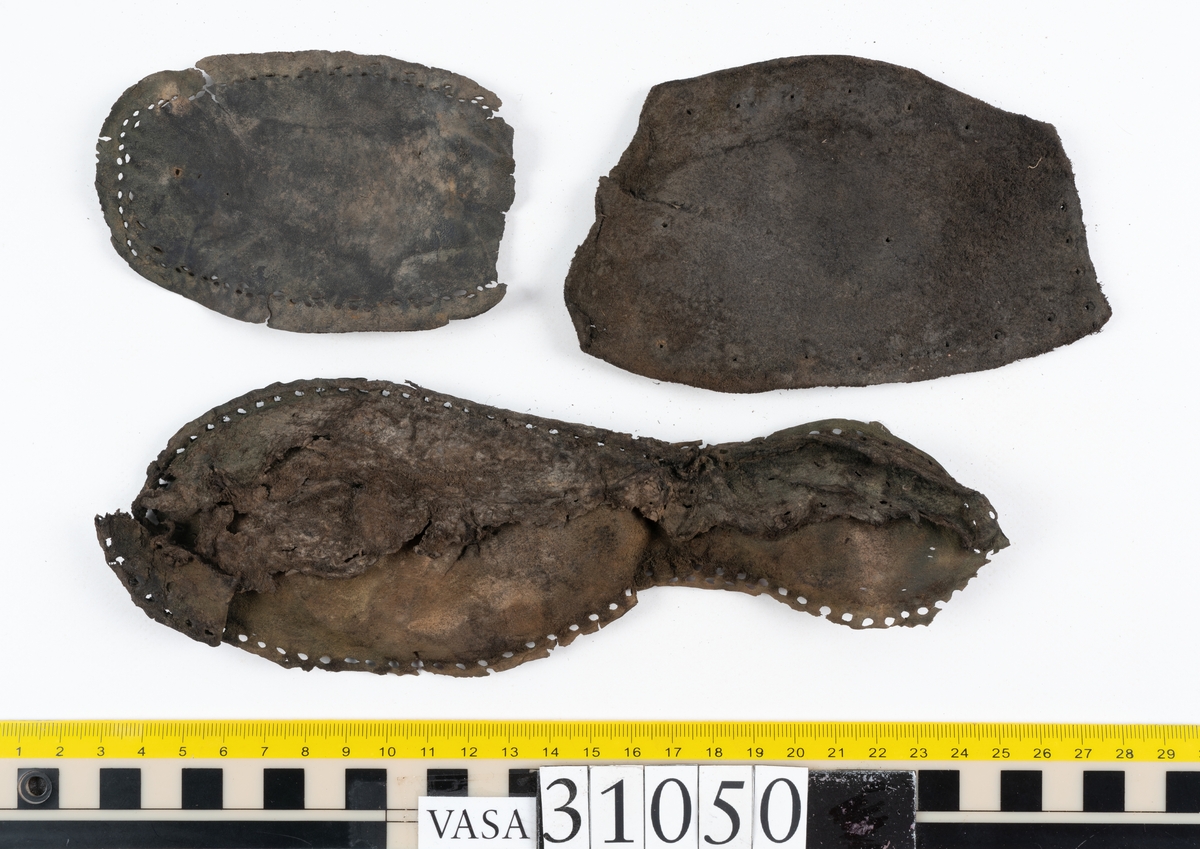 Dokumentation 1997:
Delar och fragment från sko.
Fyra sulor, fyndnummer 31050, 31050:1, 310502 samt 31050:4. Runt sulornas ytterkanter löper hål efter stygns och träpligg. Två av sulorna, fyndnummer 31050 och 31050:1, är spaltade. Lädret är mycket sprött. Sulor fyndnummer 31050:2 och 31050:3 består av ett relativt kraftigt läder. Sula fyndnummer 31050:3 är avskuren vid tåpartiet. Eventuellt kandenna sula härröra från en annan skobotten.
En bakkappa, fyndnummer 31050:4. Längs med ytterkanterna löper stygnshål. lädret är spaltat och sprött.
Ett 40-tal delar och fragment av sulor, inlägg, ovanläder mm.

Även växtfibrer.

Dokumentation 2022:
Bindsula till en svensksko. Tillverkad i läder. Inga dekorationer. Hör ihop med fyndnummer 11317. Framdelen saknas. Sättet bäraren använde skon tyder på att hen hade metatarsalgi. Det finns inga tecken på lagningar. 
För mer information, se Länkade filer: Uppritning

Text in english:
This is the insole of a shoe, made of leather, of stitch-down construction, made on a right last and worn on the right foot, with no decorative features, it pairs with 11317. The pieced front of the insole is missing and the way the weight of the wearer imprinted on the insole suggests that they had a depressed transverse metatarsal arch. There are no signs of repairs.
For more information, go to Länkade filer: Uppritning
