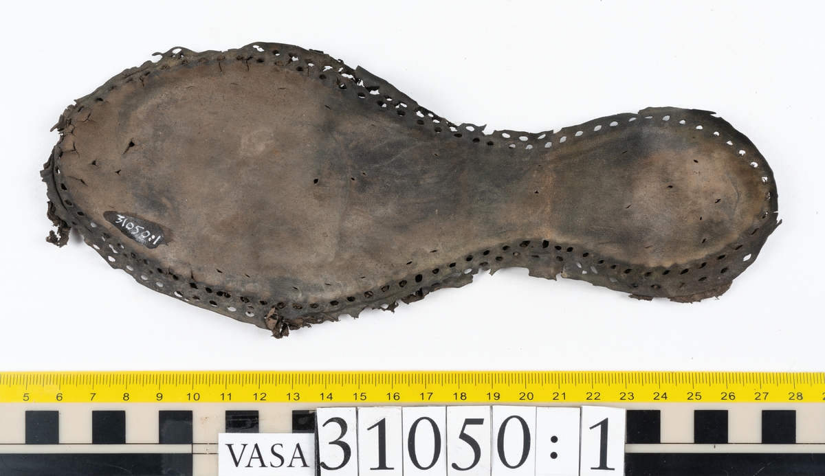 Dokumentation 1997:
Delar och fragment från sko.
Fyra sulor, fyndnummer 31050, 31050:1, 310502 samt 31050:4. Runt sulornas ytterkanter löper hål efter stygns och träpligg. Två av sulorna, fyndnummer 31050 och 31050:1, är spaltade. Lädret är mycket sprött. Sulor fyndnummer 31050:2 och 31050:3 består av ett relativt kraftigt läder. Sula fyndnummer 31050:3 är avskuren vid tåpartiet. Eventuellt kandenna sula härröra från en annan skobotten.
En bakkappa, fyndnummer 31050:4. Längs med ytterkanterna löper stygnshål. lädret är spaltat och sprött.
Ett 40-tal delar och fragment av sulor, inlägg, ovanläder mm.

Även växtfibrer.

Dokumentation 2022:
Bindsula till en svensksko. Tillverkad i läder. Inga dekorationer. Hör ihop med fyndnummer 11317. Framdelen saknas. Sättet bäraren använde skon tyder på att hen hade metatarsalgi. Det finns inga tecken på lagningar. 
För mer information, se Länkade filer: Uppritning

Text in english:
This is the insole of a shoe, made of leather, of stitch-down construction, made on a right last and worn on the right foot, with no decorative features, it pairs with 11317. The pieced front of the insole is missing and the way the weight of the wearer imprinted on the insole suggests that they had a depressed transverse metatarsal arch. There are no signs of repairs.
For more information, go to Länkade filer: Uppritning