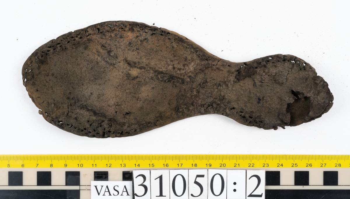 Dokumentation 1997:
Delar och fragment från sko.
Fyra sulor, fyndnummer 31050, 31050:1, 310502 samt 31050:4. Runt sulornas ytterkanter löper hål efter stygns och träpligg. Två av sulorna, fyndnummer 31050 och 31050:1, är spaltade. Lädret är mycket sprött. Sulor fyndnummer 31050:2 och 31050:3 består av ett relativt kraftigt läder. Sula fyndnummer 31050:3 är avskuren vid tåpartiet. Eventuellt kandenna sula härröra från en annan skobotten.
En bakkappa, fyndnummer 31050:4. Längs med ytterkanterna löper stygnshål. lädret är spaltat och sprött.
Ett 40-tal delar och fragment av sulor, inlägg, ovanläder mm.

Även växtfibrer.

Dokumentation 2022:
Bindsula till en svensksko. Tillverkad i läder. Inga dekorationer. Hör ihop med fyndnummer 11317. Framdelen saknas. Sättet bäraren använde skon tyder på att hen hade metatarsalgi. Det finns inga tecken på lagningar. 
För mer information, se Länkade filer: Uppritning

Text in english:
This is the insole of a shoe, made of leather, of stitch-down construction, made on a right last and worn on the right foot, with no decorative features, it pairs with 11317. The pieced front of the insole is missing and the way the weight of the wearer imprinted on the insole suggests that they had a depressed transverse metatarsal arch. There are no signs of repairs.
For more information, go to Länkade filer: Uppritning
