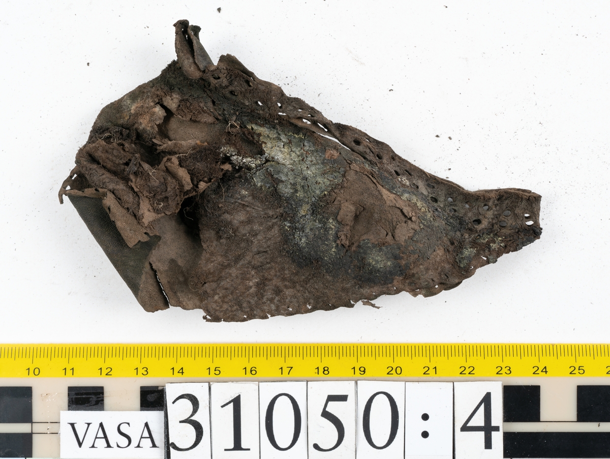Dokumentation 1997:
Delar och fragment från sko.
Fyra sulor, fyndnummer 31050, 31050:1, 310502 samt 31050:4. Runt sulornas ytterkanter löper hål efter stygns och träpligg. Två av sulorna, fyndnummer 31050 och 31050:1, är spaltade. Lädret är mycket sprött. Sulor fyndnummer 31050:2 och 31050:3 består av ett relativt kraftigt läder. Sula fyndnummer 31050:3 är avskuren vid tåpartiet. Eventuellt kandenna sula härröra från en annan skobotten.
En bakkappa, fyndnummer 31050:4. Längs med ytterkanterna löper stygnshål. lädret är spaltat och sprött.
Ett 40-tal delar och fragment av sulor, inlägg, ovanläder mm.

Även växtfibrer.

Dokumentation 2022:
Bindsula till en svensksko. Tillverkad i läder. Inga dekorationer. Hör ihop med fyndnummer 11317. Framdelen saknas. Sättet bäraren använde skon tyder på att hen hade metatarsalgi. Det finns inga tecken på lagningar. 
För mer information, se Länkade filer: Uppritning

Text in english:
This is the insole of a shoe, made of leather, of stitch-down construction, made on a right last and worn on the right foot, with no decorative features, it pairs with 11317. The pieced front of the insole is missing and the way the weight of the wearer imprinted on the insole suggests that they had a depressed transverse metatarsal arch. There are no signs of repairs.
For more information, go to Länkade filer: Uppritning