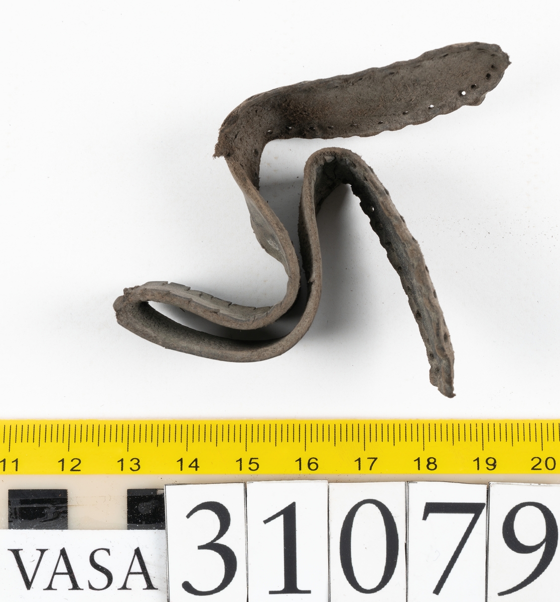 Två delar tillhörande en stövel: en stropp samt en del av en stropp från ett stövelskaft.

Den ena stroppen ligger dubbelvikt. I två av ändarna finns stygnshål efter fastsättningen. Lädret är välbevarat.

Den andra stroppen är fragmentarisk. I ena änden finns stygnshål i forman av en rektangel. Lädret är sprucket och något spaltat.