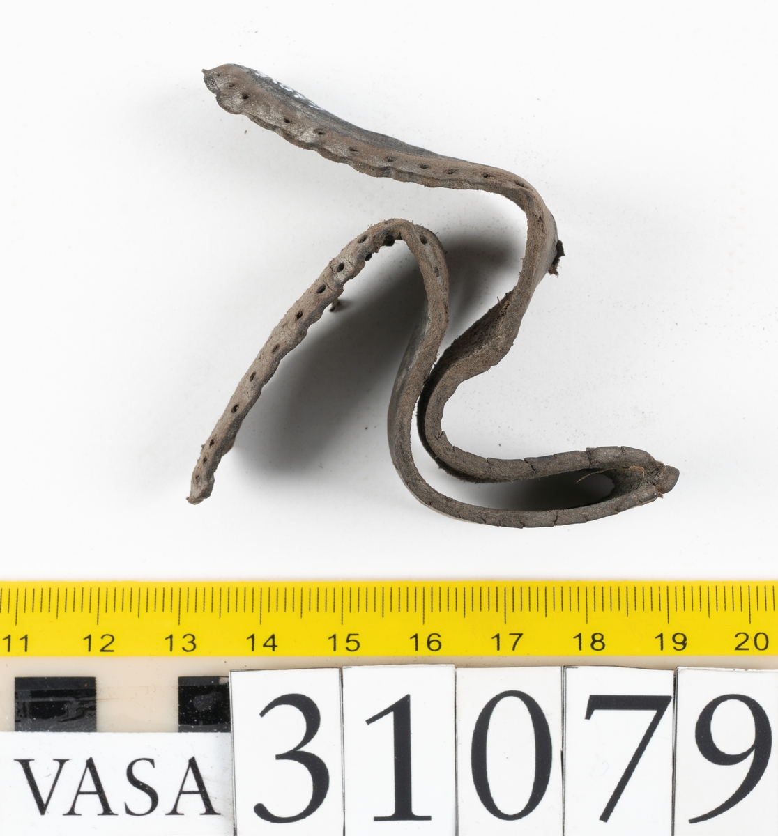 Två delar tillhörande en stövel: en stropp samt en del av en stropp från ett stövelskaft.

Den ena stroppen ligger dubbelvikt. I två av ändarna finns stygnshål efter fastsättningen. Lädret är välbevarat.

Den andra stroppen är fragmentarisk. I ena änden finns stygnshål i forman av en rektangel. Lädret är sprucket och något spaltat.