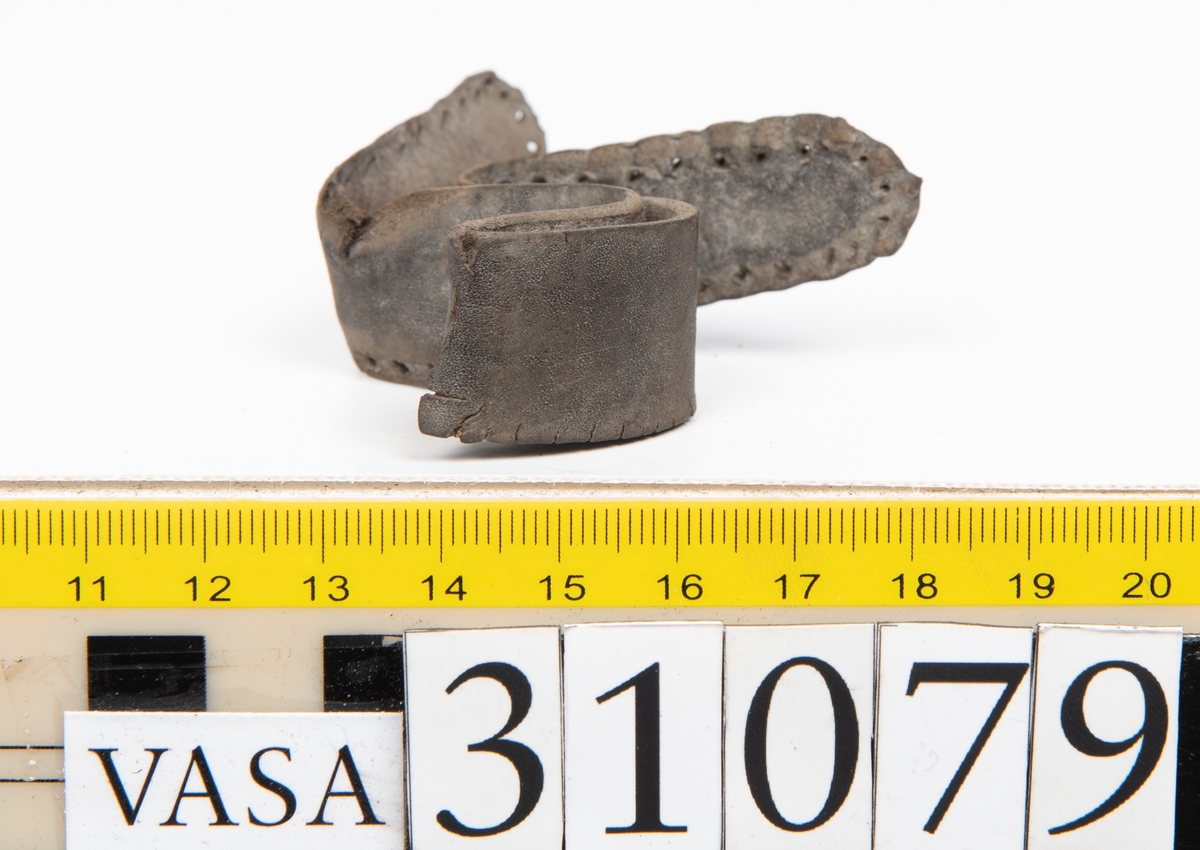 Två delar tillhörande en stövel: en stropp samt en del av en stropp från ett stövelskaft.

Den ena stroppen ligger dubbelvikt. I två av ändarna finns stygnshål efter fastsättningen. Lädret är välbevarat.

Den andra stroppen är fragmentarisk. I ena änden finns stygnshål i forman av en rektangel. Lädret är sprucket och något spaltat.